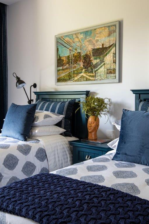 Two twin beds with navy blue wooden headboards and patterned blue and white linens flank a central dark blue nightstand.