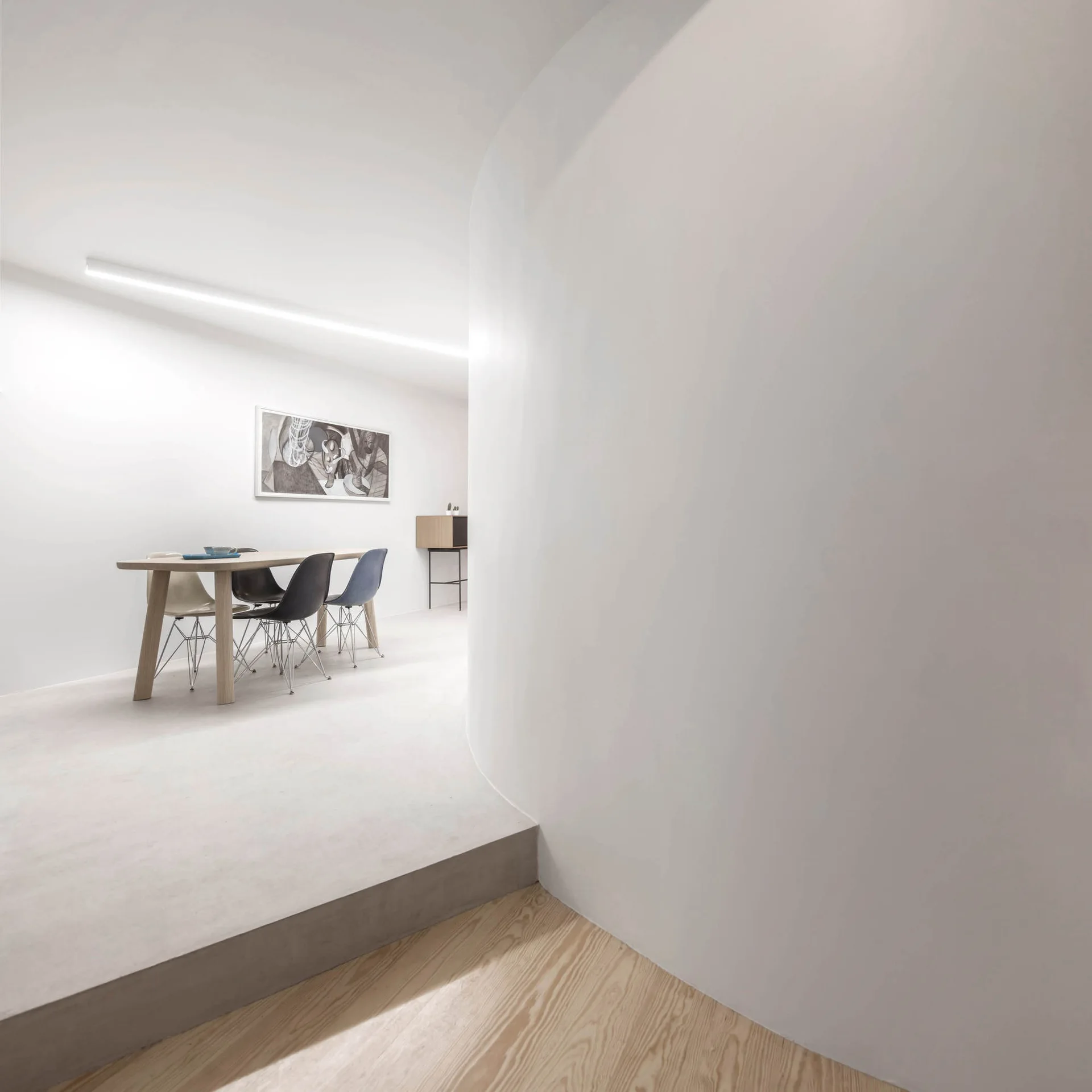 A minimalist dining area on a raised concrete platform features a wooden table, plastic chairs, and a large curved white partition wall.
