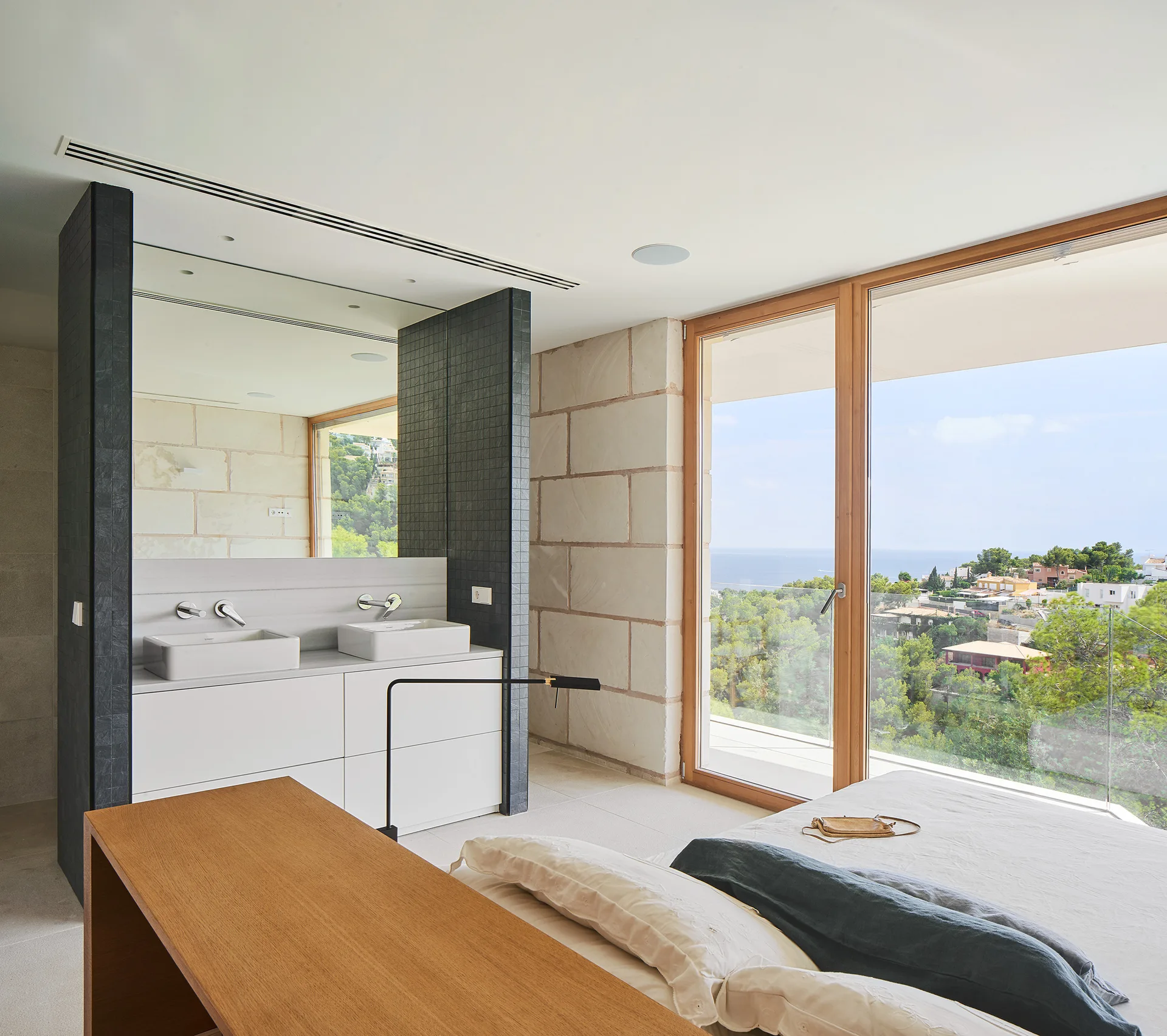 A contemporary bedroom features an integrated white vanity cabinet and large stone block walls next to sliding glass doors.