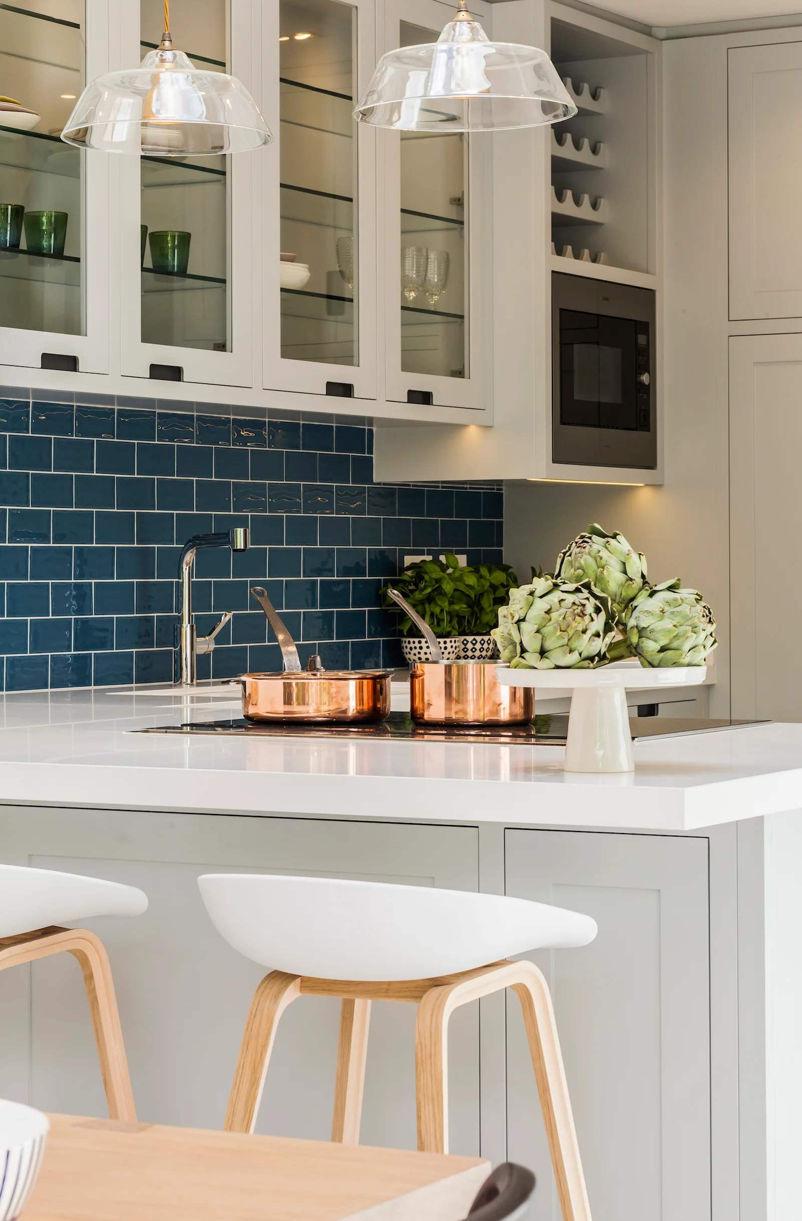 A modern white kitchen features shaker-style cabinets, a glossy navy blue tile backsplash, and a white kitchen island with copper pots on the stovetop.