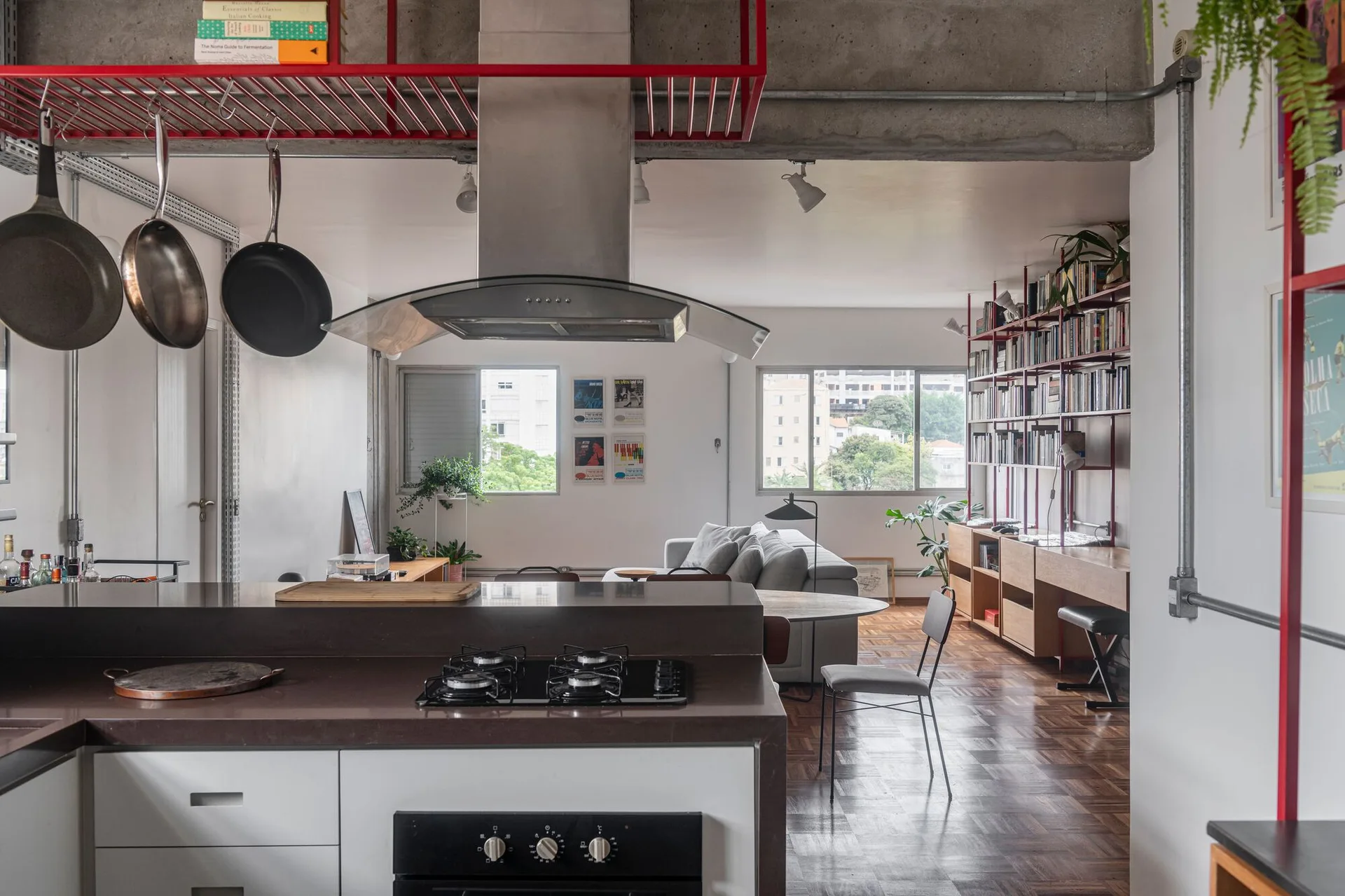 An open plan kitchen and living space featuring a dark countertop island, a red hanging metal rack, and parquet wood floors.
