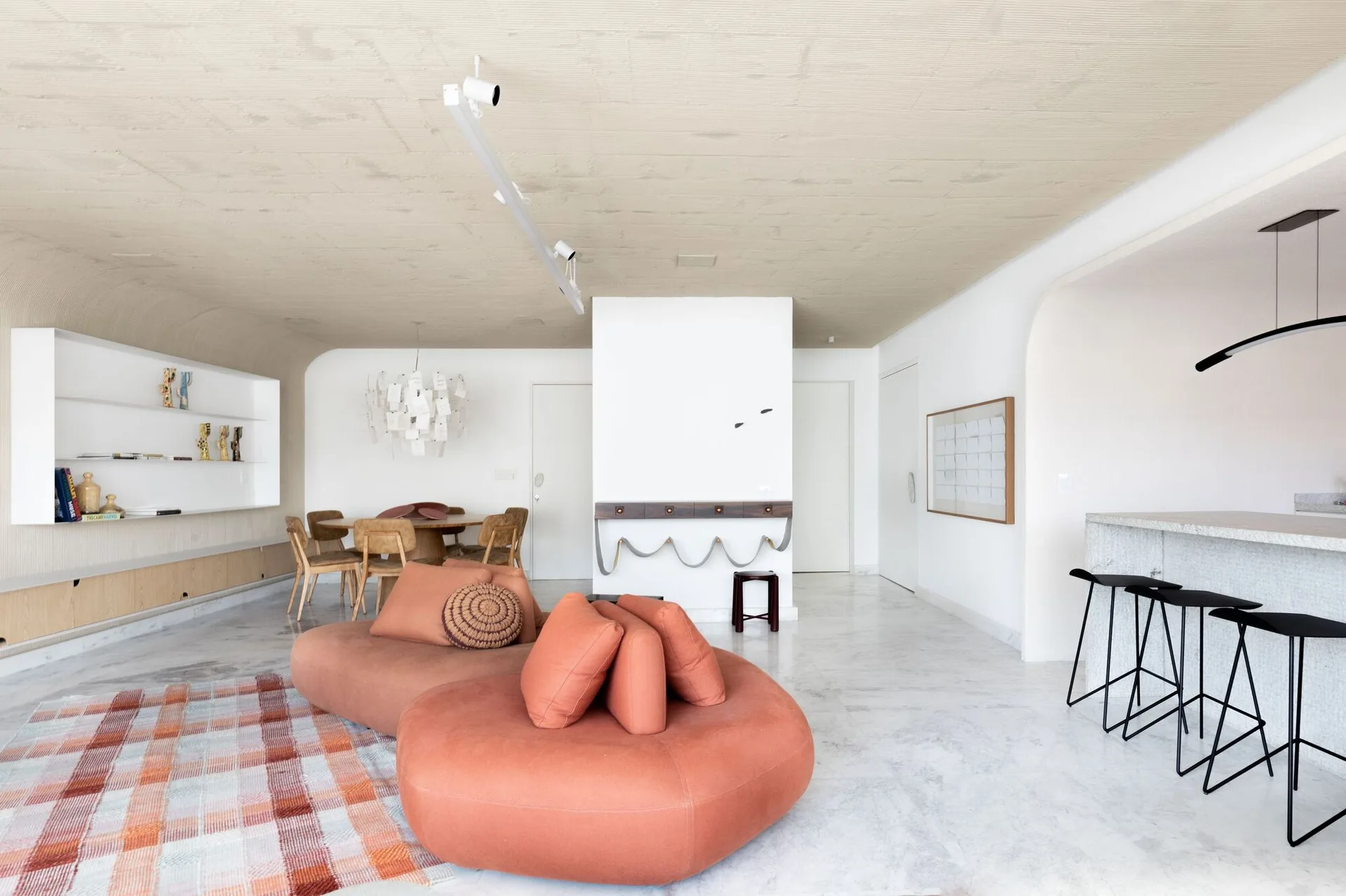 A spacious open-concept living room features a curved orange sofa, a plaid rug, a stone bar counter, and a textured coved ceiling.