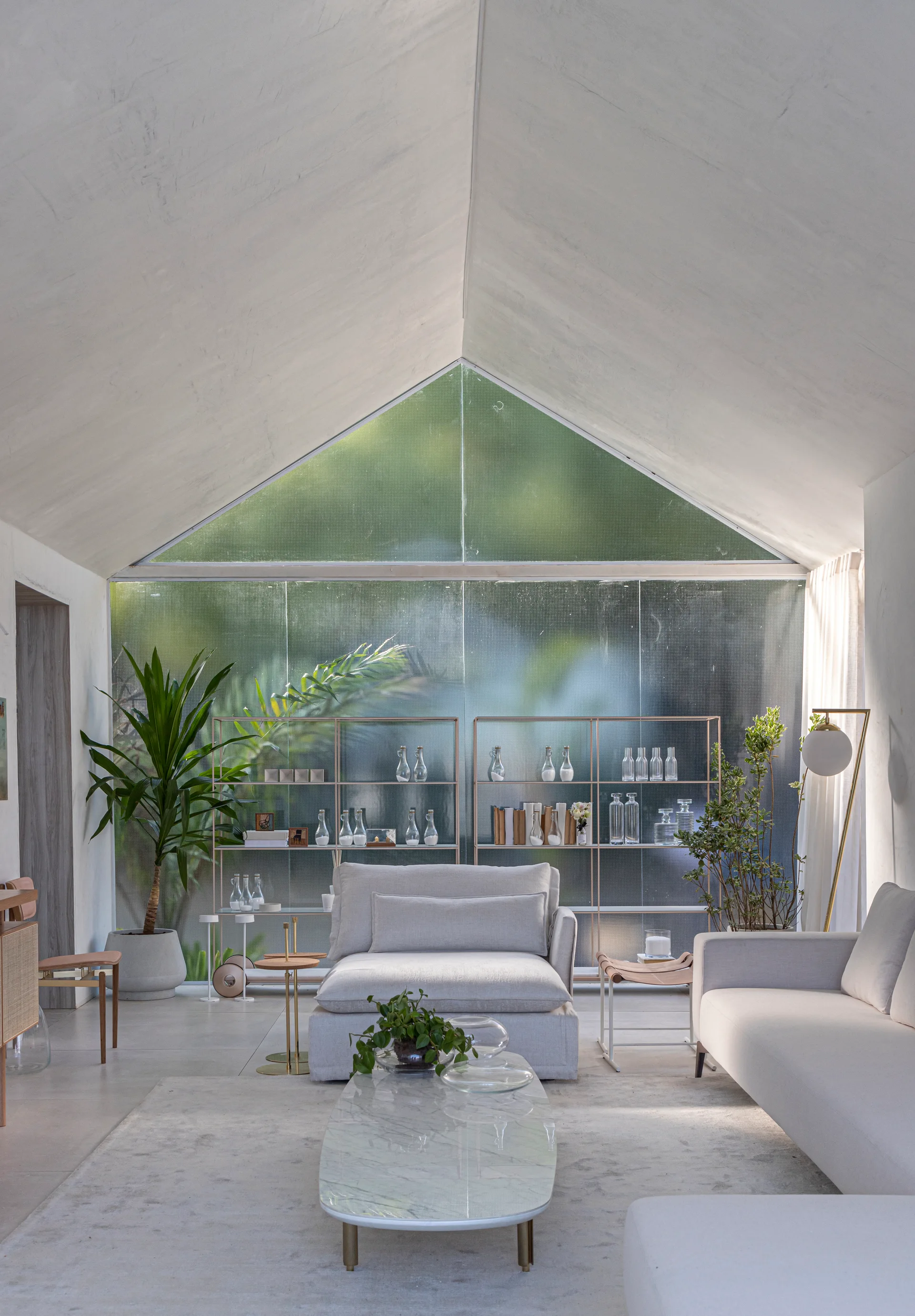 A bright living room featuring a vaulted ceiling, a large textured glass window looking onto greenery, and light grey contemporary sofas.