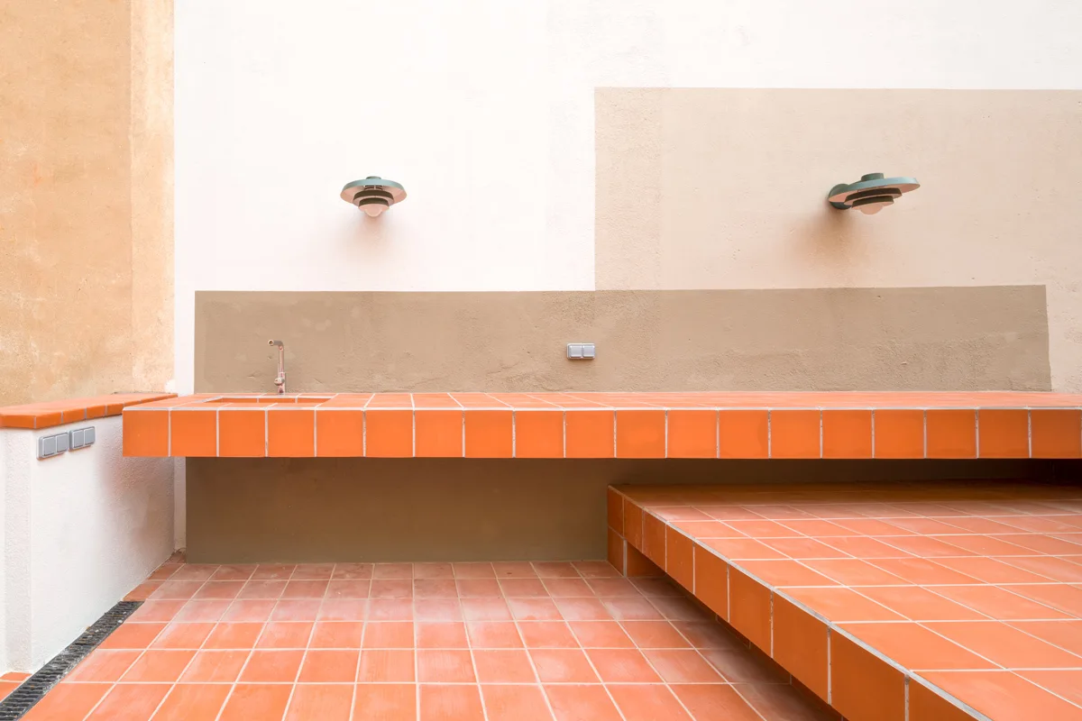 An outdoor kitchen area features a long counter and tiered platform covered in orange ceramic tiles against a color-blocked stucco wall.