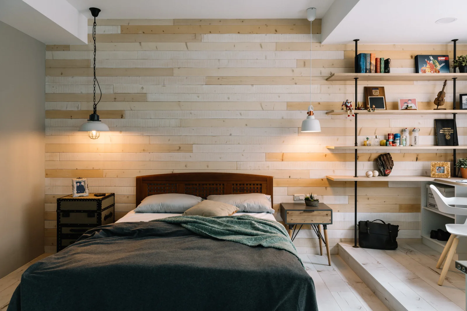 A contemporary bedroom features a horizontal light wood plank feature wall, a platform bed, and a raised floor platform with integrated workspace shelving.