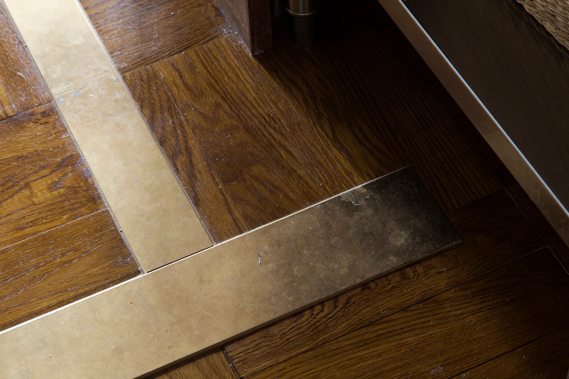 A close-up view of dark-stained wood parquet flooring featuring flat brass metal strip inlays embedded between the wood tiles.