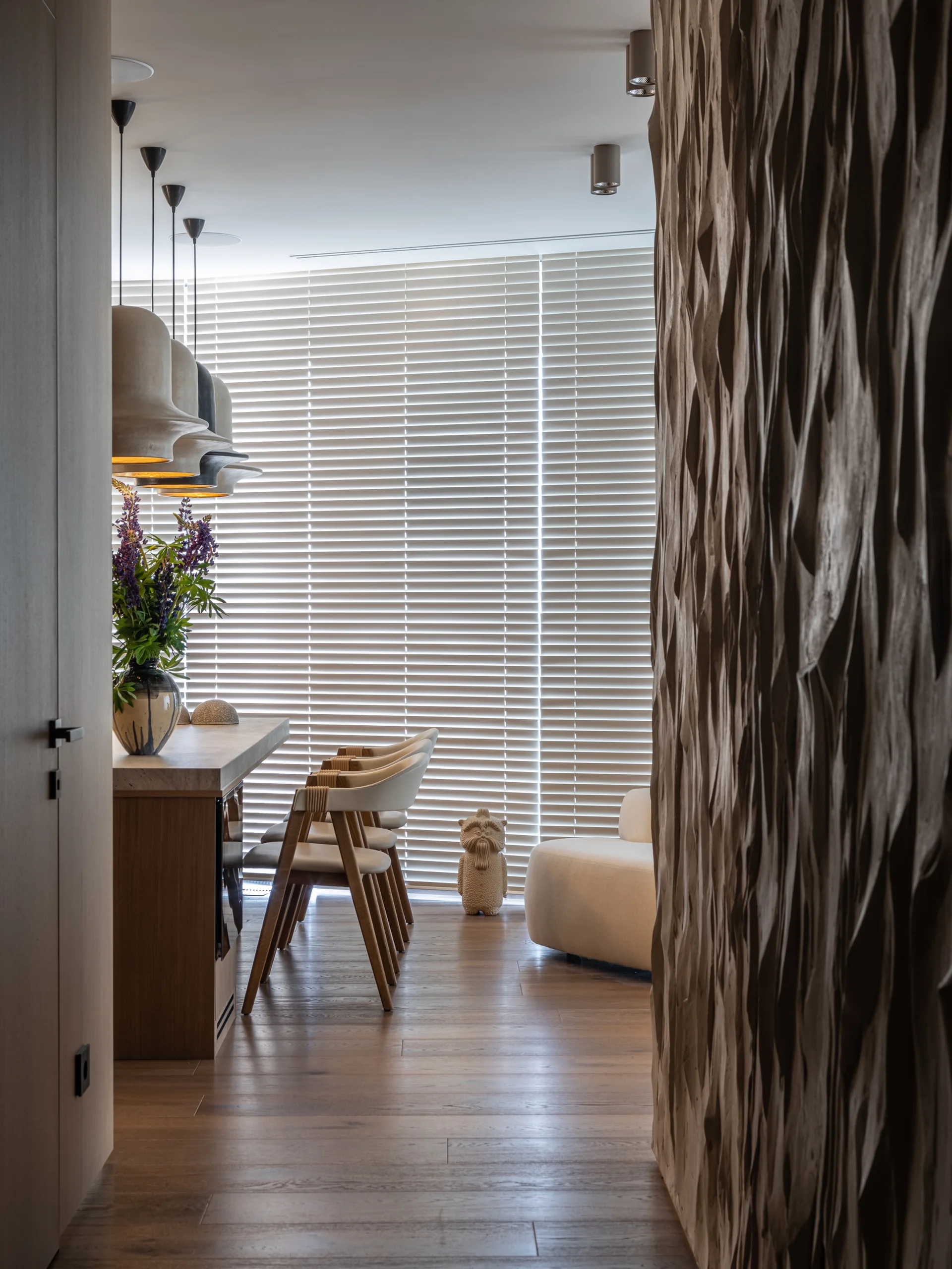 A modern dining room features a textured wood accent wall, a stone-topped table with white chairs, and large horizontal window blinds.
