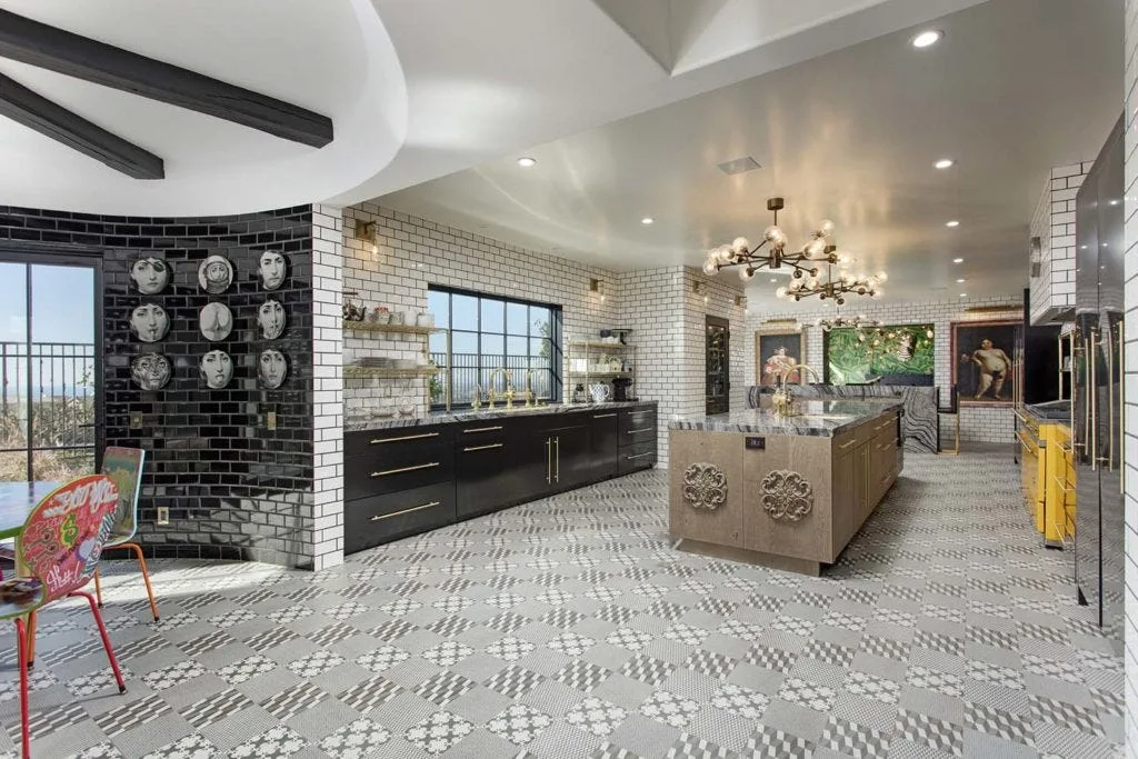 A spacious kitchen features a patterned geometric tile floor, a wood island with a stone top, dark lower cabinets, and a curved black subway tile wall.