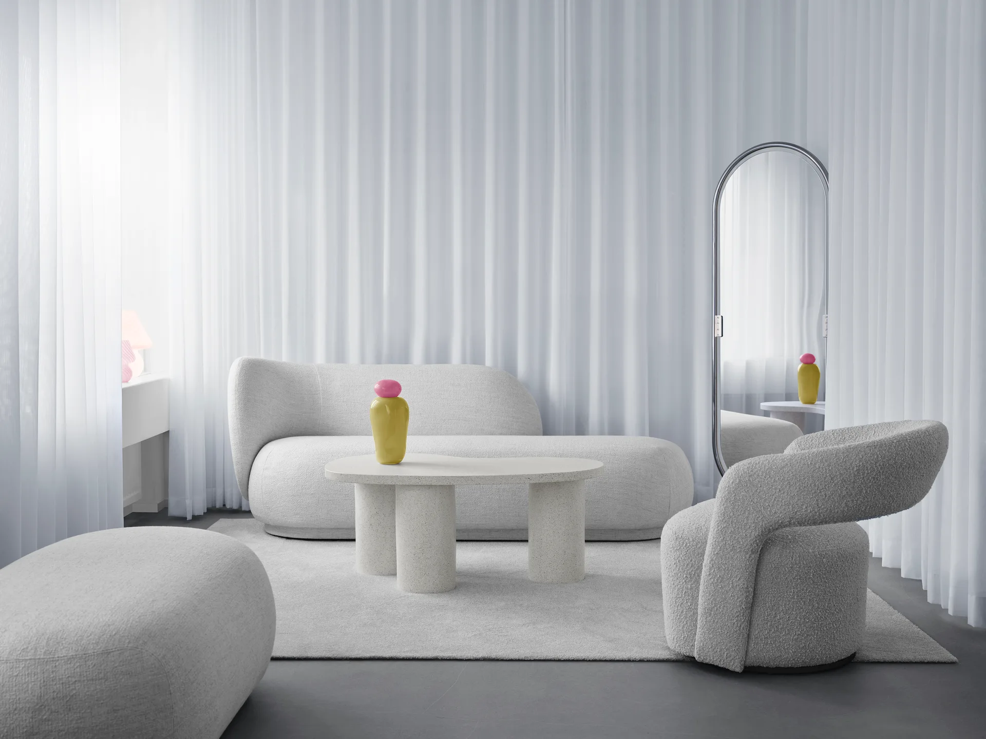 A minimalist white living room featuring curved boucle furniture, a flecked terrazzo table, and an arched mirror against sheer floor-to-ceiling curtains.