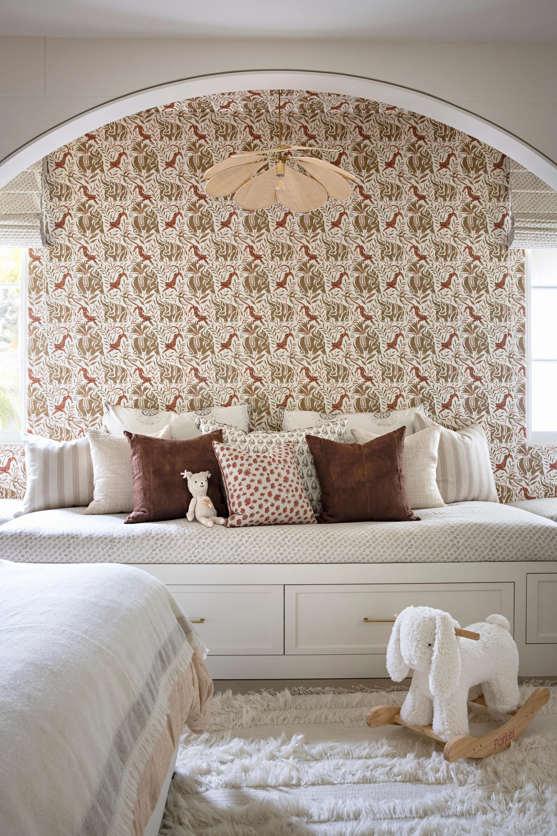 A white built-in daybed with terracotta throw pillows sits inside a patterned wallpapered archway.