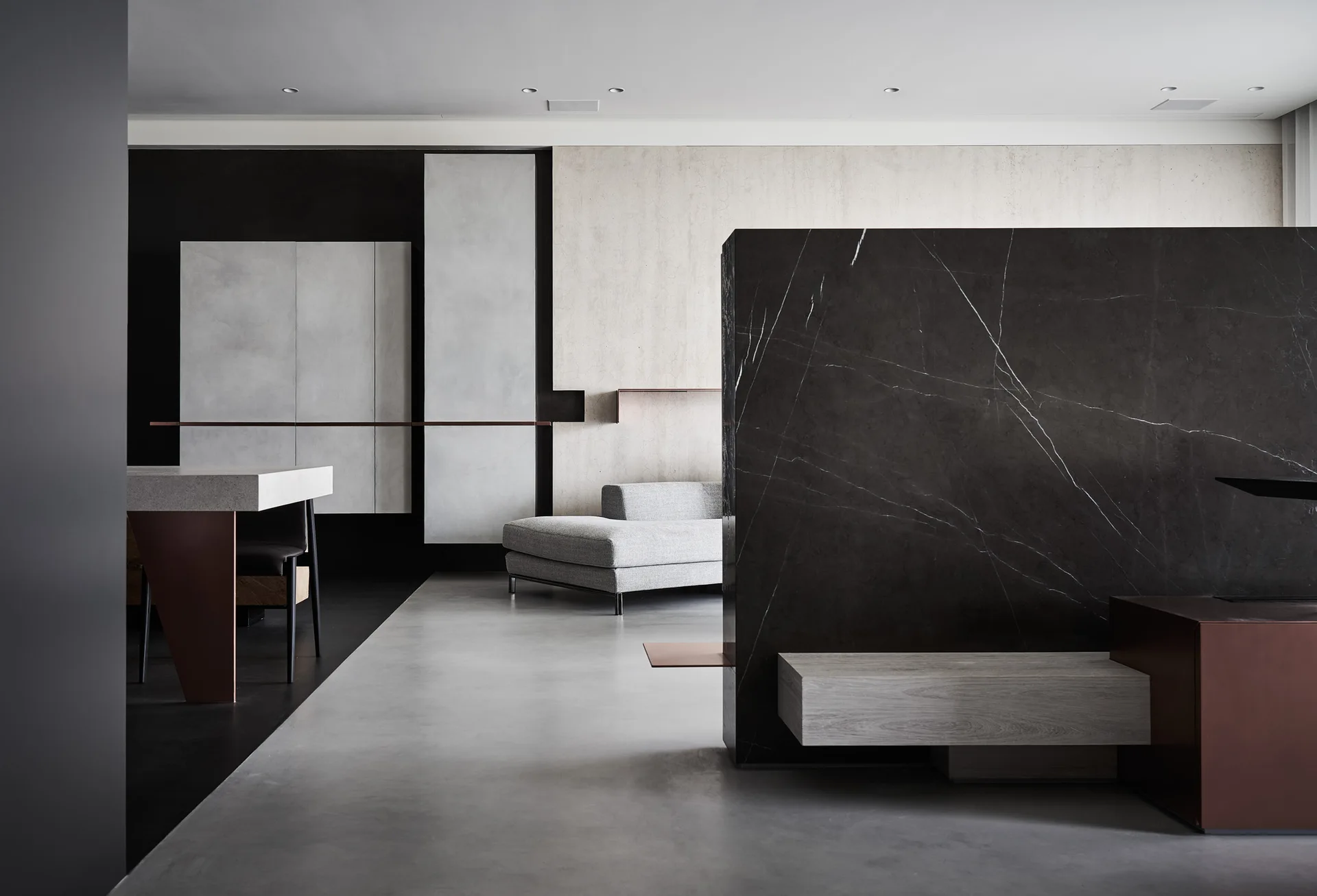 A minimalist open living room with a large dark marble partition wall, light grey concrete floor, and low profile furniture.