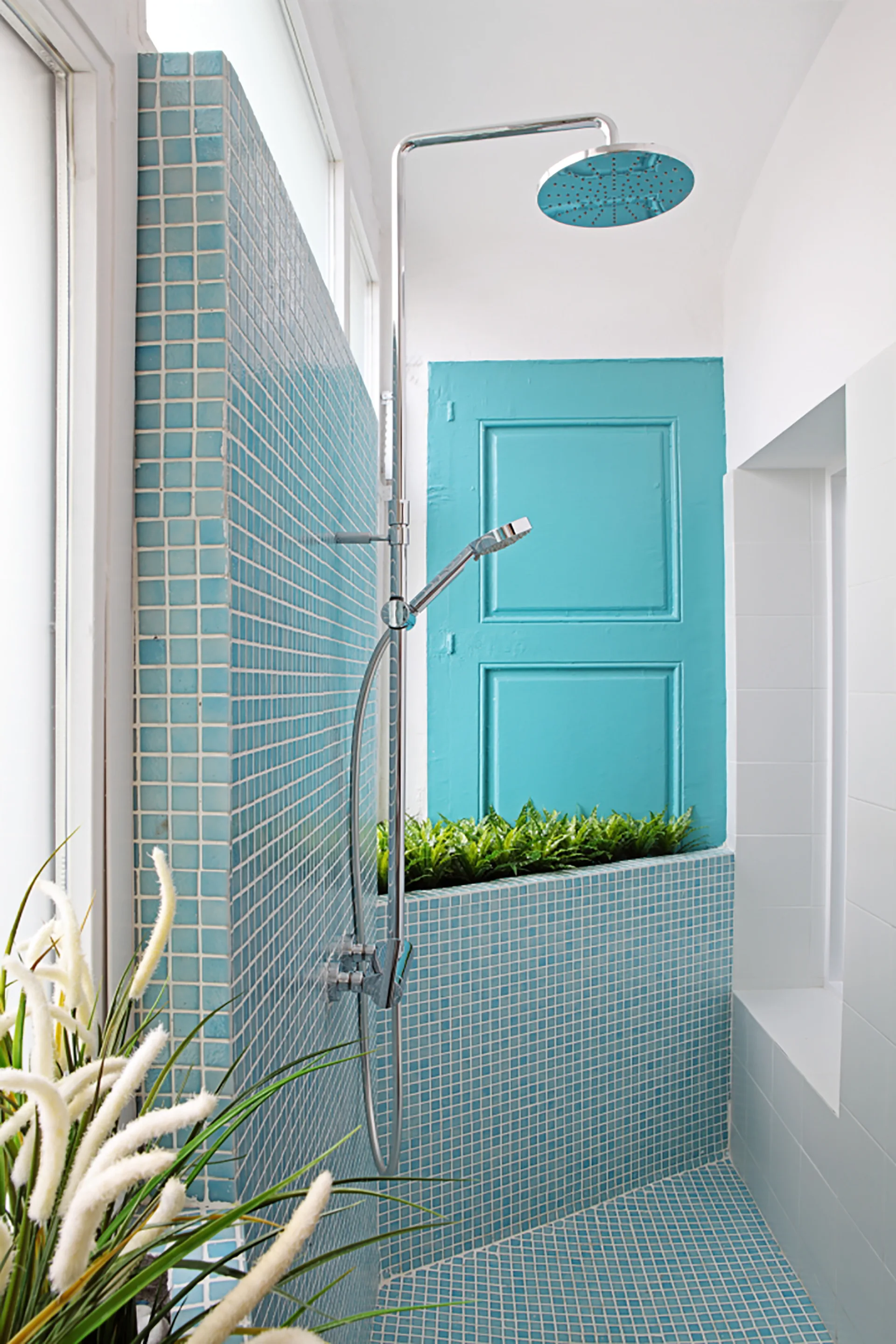 A bright shower area features vibrant turquoise mosaic tiling on the walls and floor, a chrome rainfall shower head, and a painted blue door.