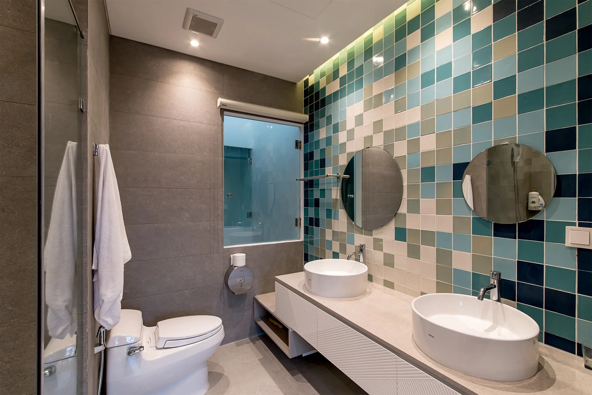 A modern bathroom featuring a double vanity with white vessel sinks and circular mirrors against a blue and green square tiled wall.