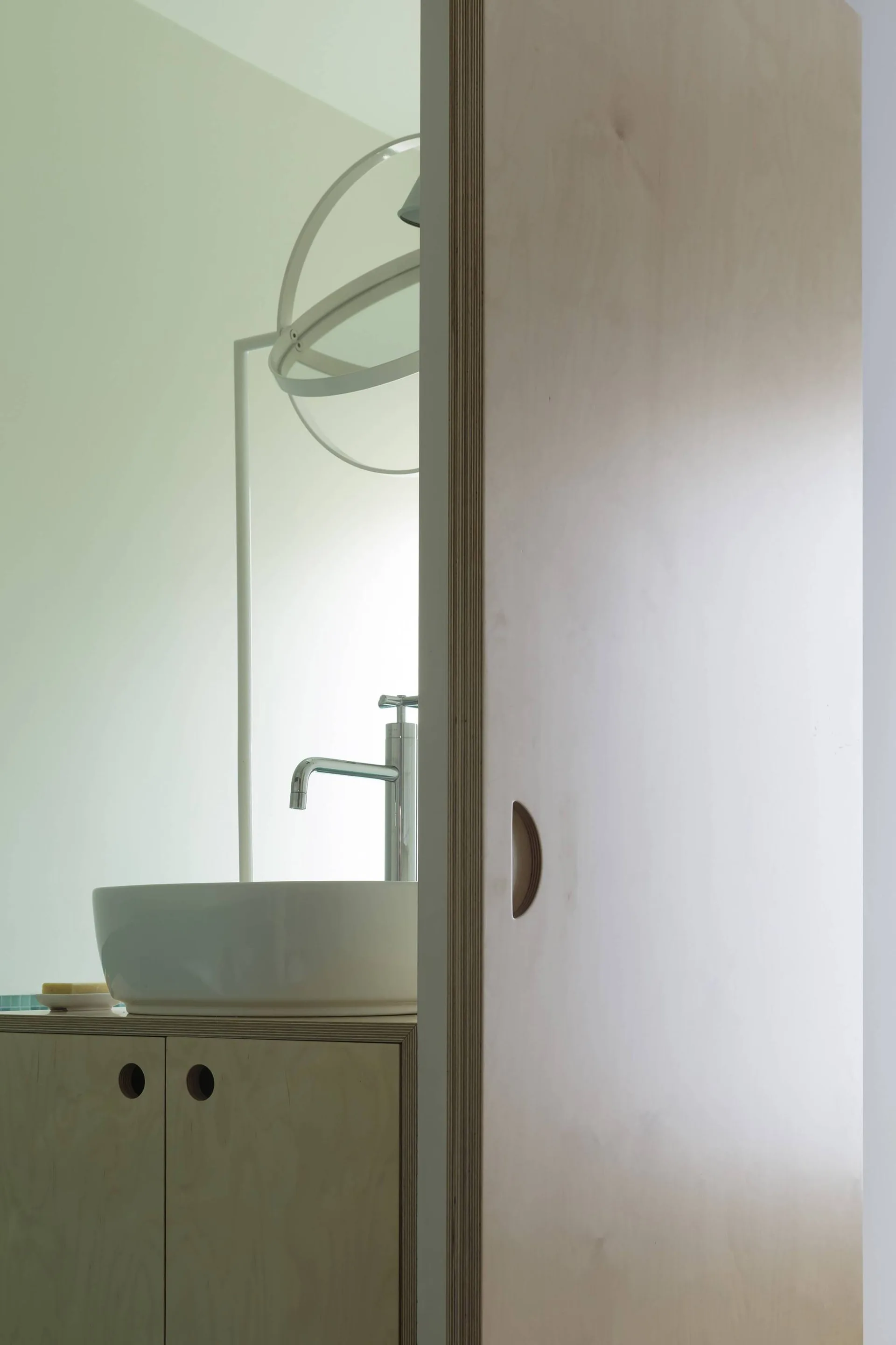 A modern bathroom vanity featuring a white vessel sink and light-toned plywood cabinetry next to a matching sliding plywood door.