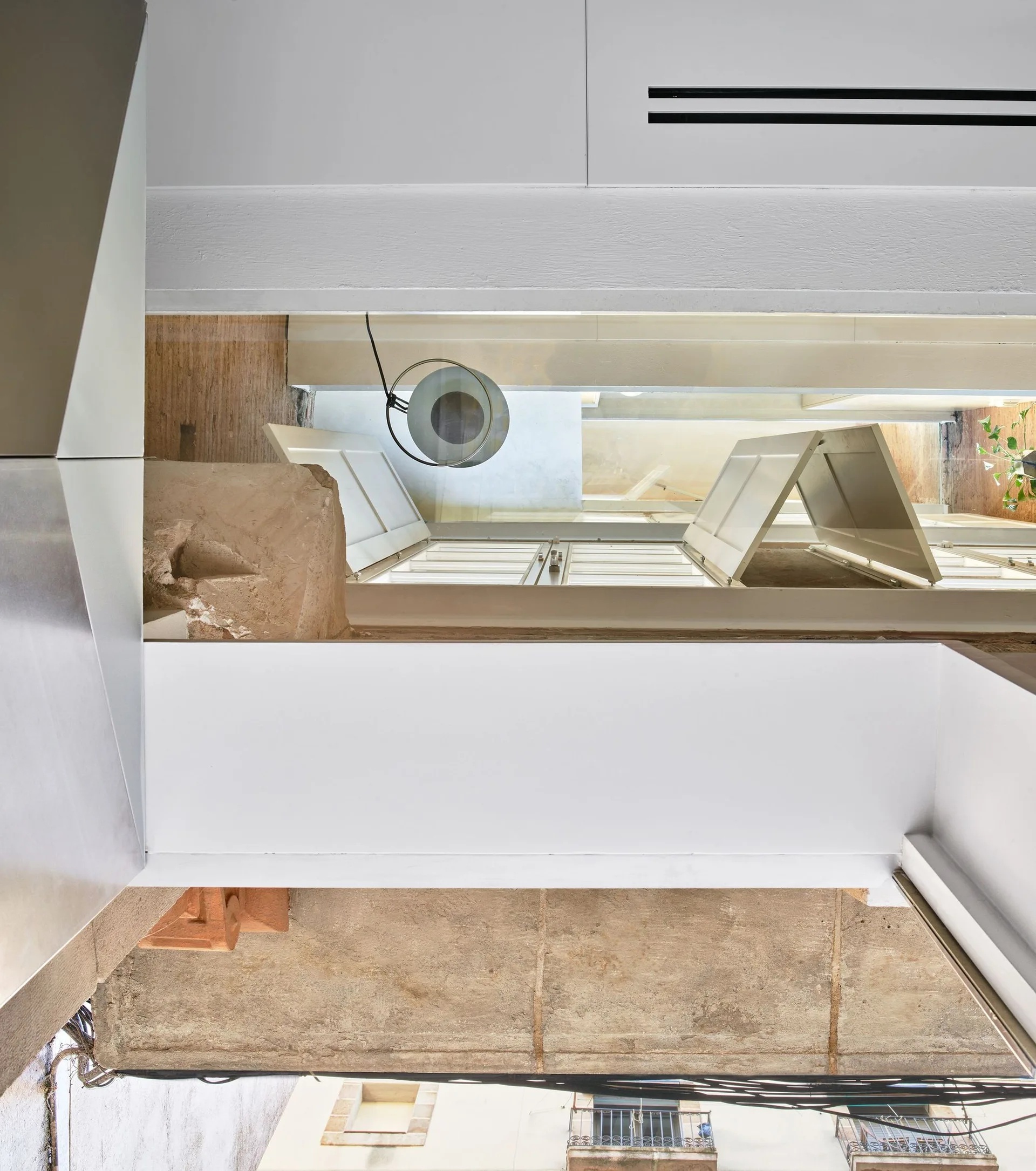 A bright transitional kitchen space features minimalist white cabinetry alongside a rough stone wall and a window with white shutters.