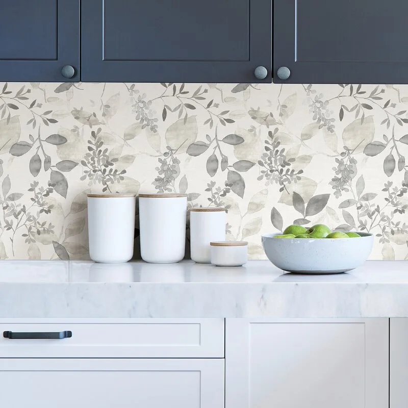 A kitchen counter with a gray botanical leaf pattern backsplash, dark upper cabinets, white lower cabinets, and ceramic canisters on a marble countertop.
