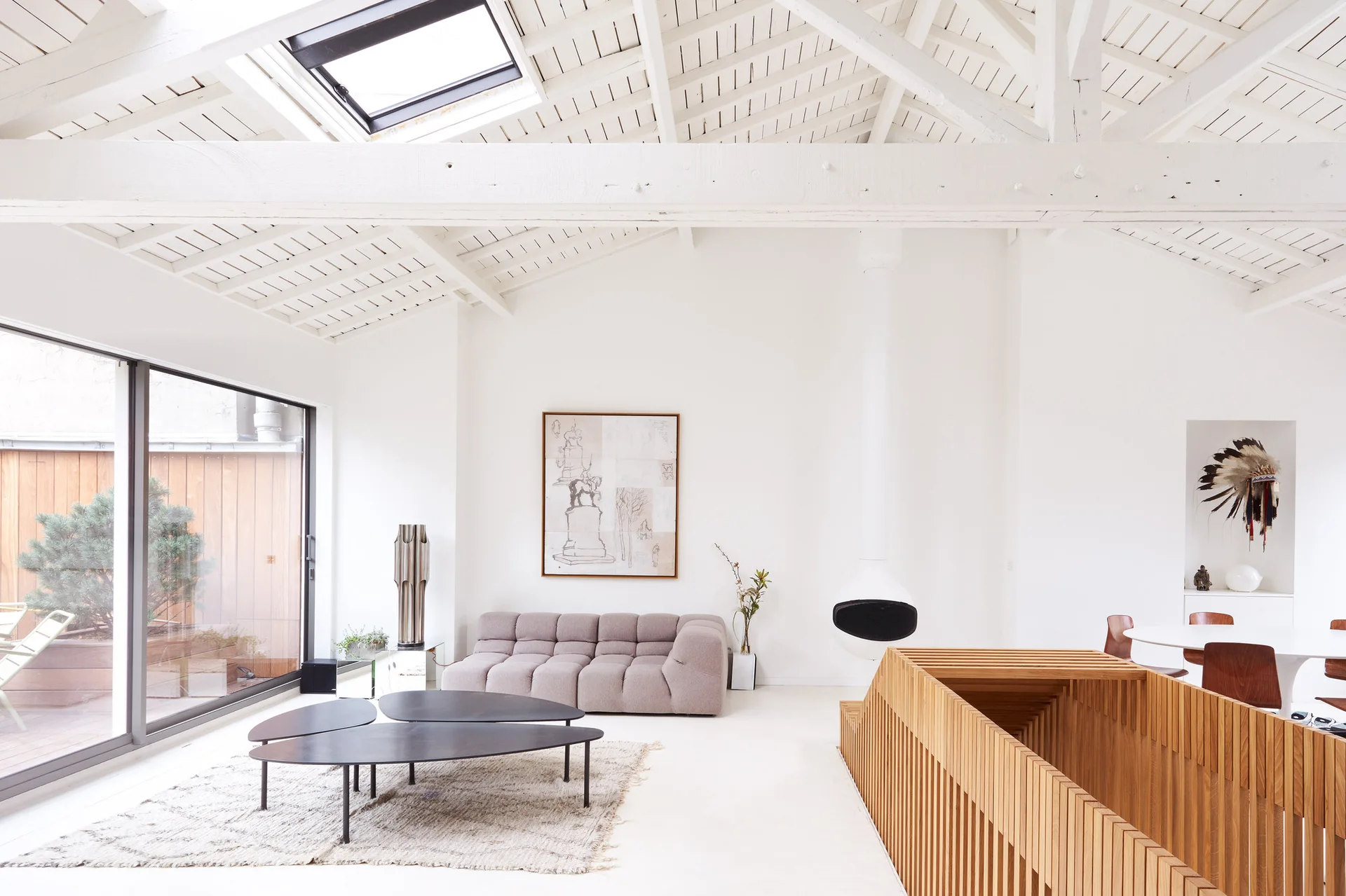 A bright loft living room featuring a low-profile modular sofa, black organic coffee tables, and a white suspended fireplace under a beamed ceiling.