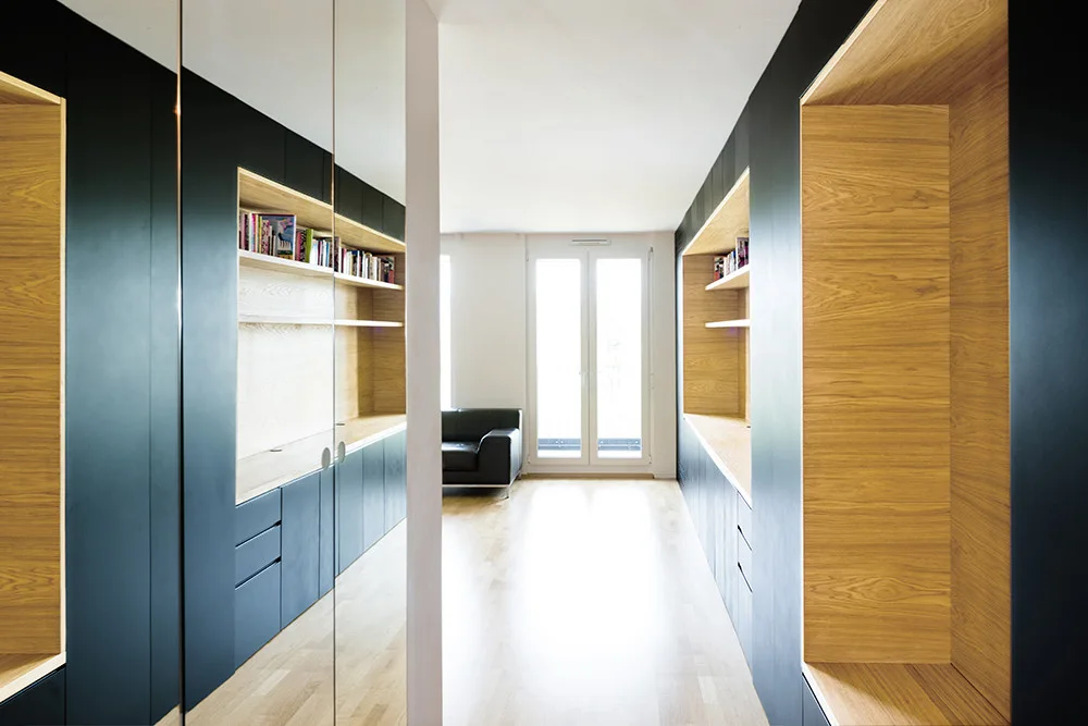 A modern residential hallway featuring matte black floor-to-ceiling built-in cabinets with recessed light wood shelving and mirrored doors.