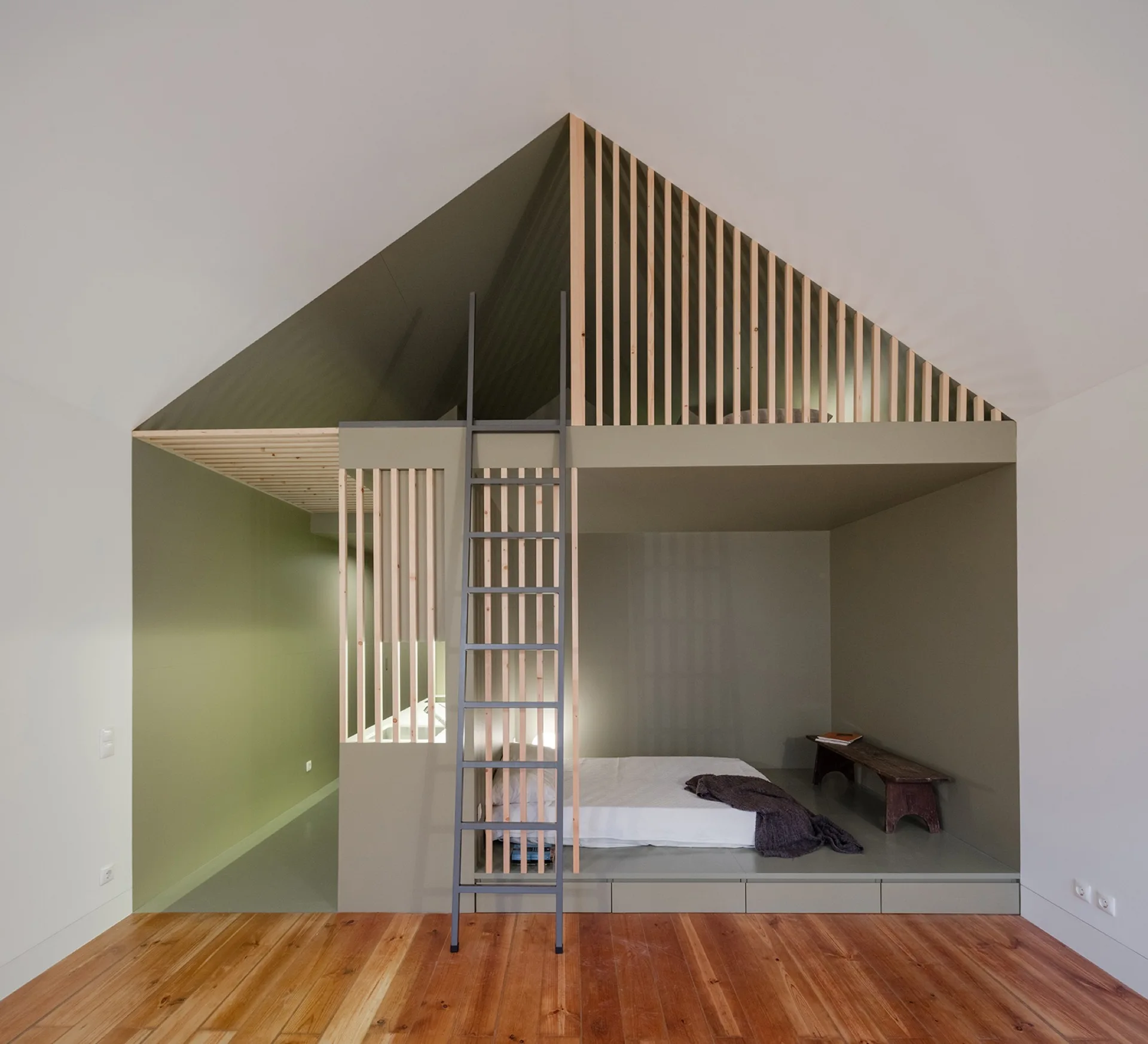 A sage green built-in sleeping alcove features a lower bed platform, a grey ladder leading to an upper loft, and vertical light wood slat screens.