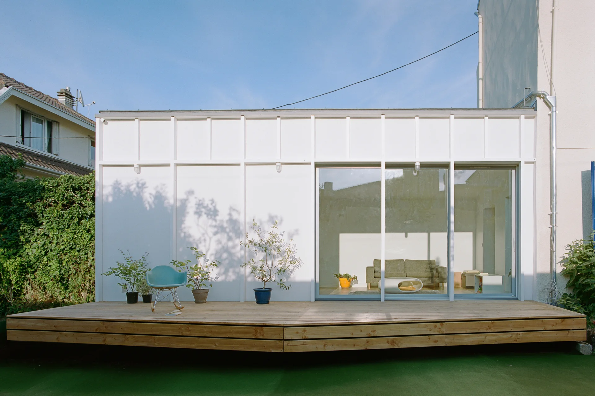 A raised wooden deck sits in front of a white paneled building featuring large sliding glass doors and a blue rocking chair.