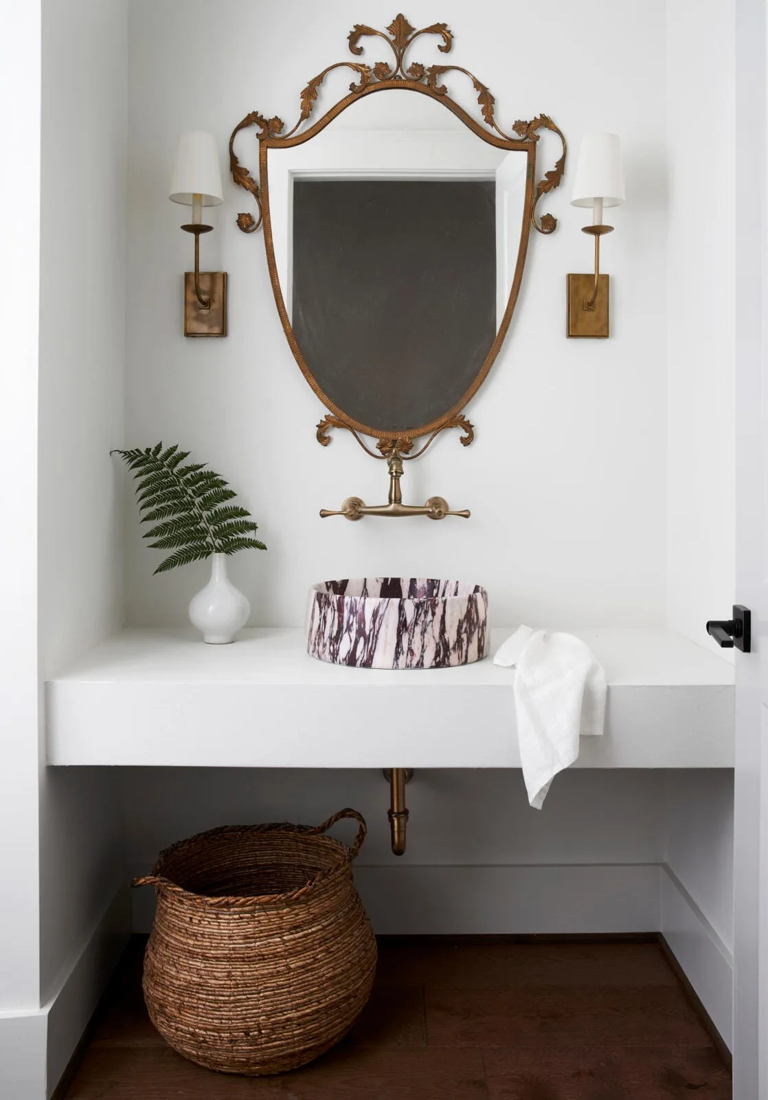 A powder room features a purple-veined marble vessel sink on a white floating vanity under an ornate gold mirror and wall-mounted brass faucet.