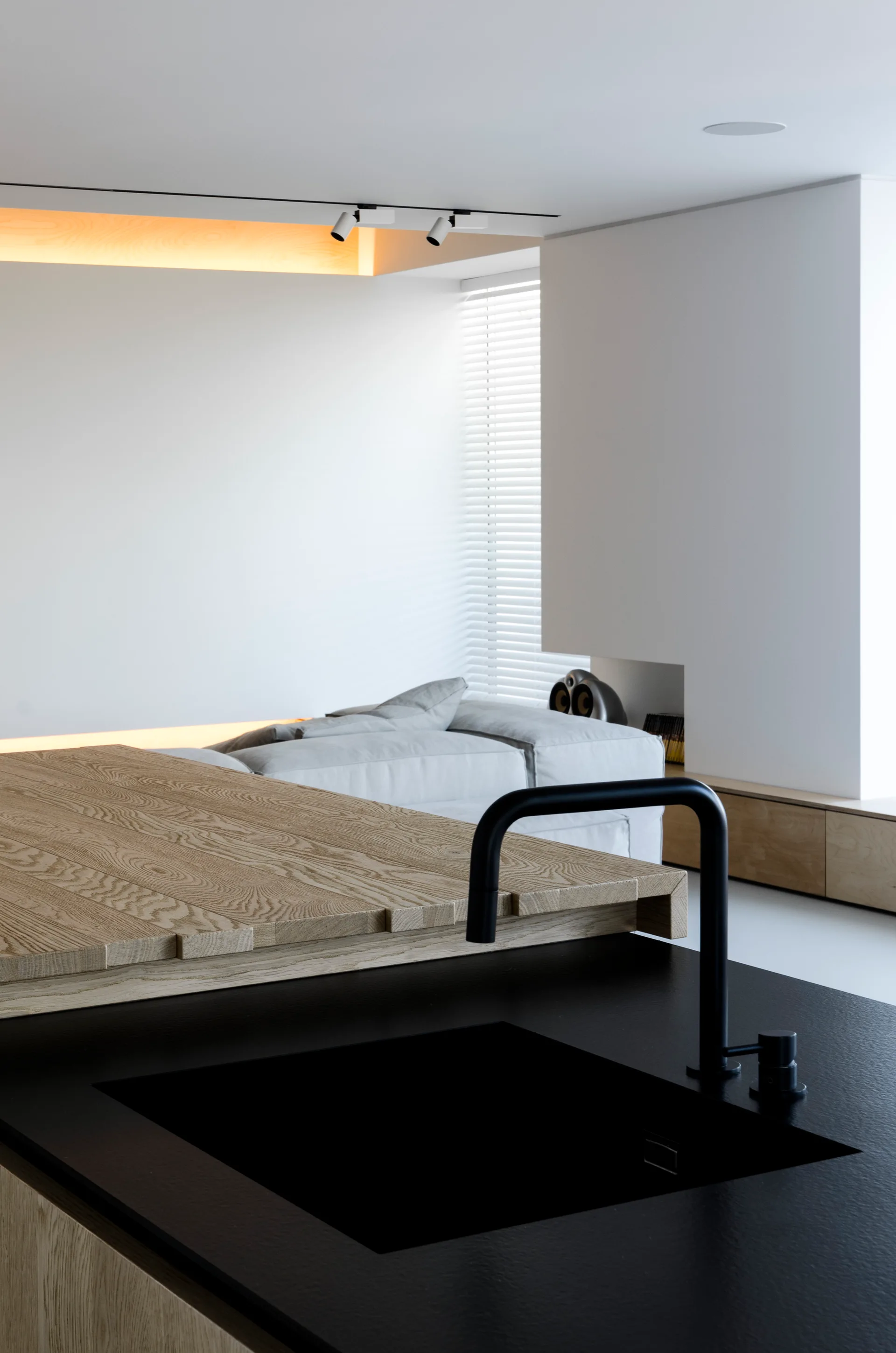 A minimalist kitchen island featuring a matte black countertop, matching black faucet, and an integrated light oak wood counter extension.