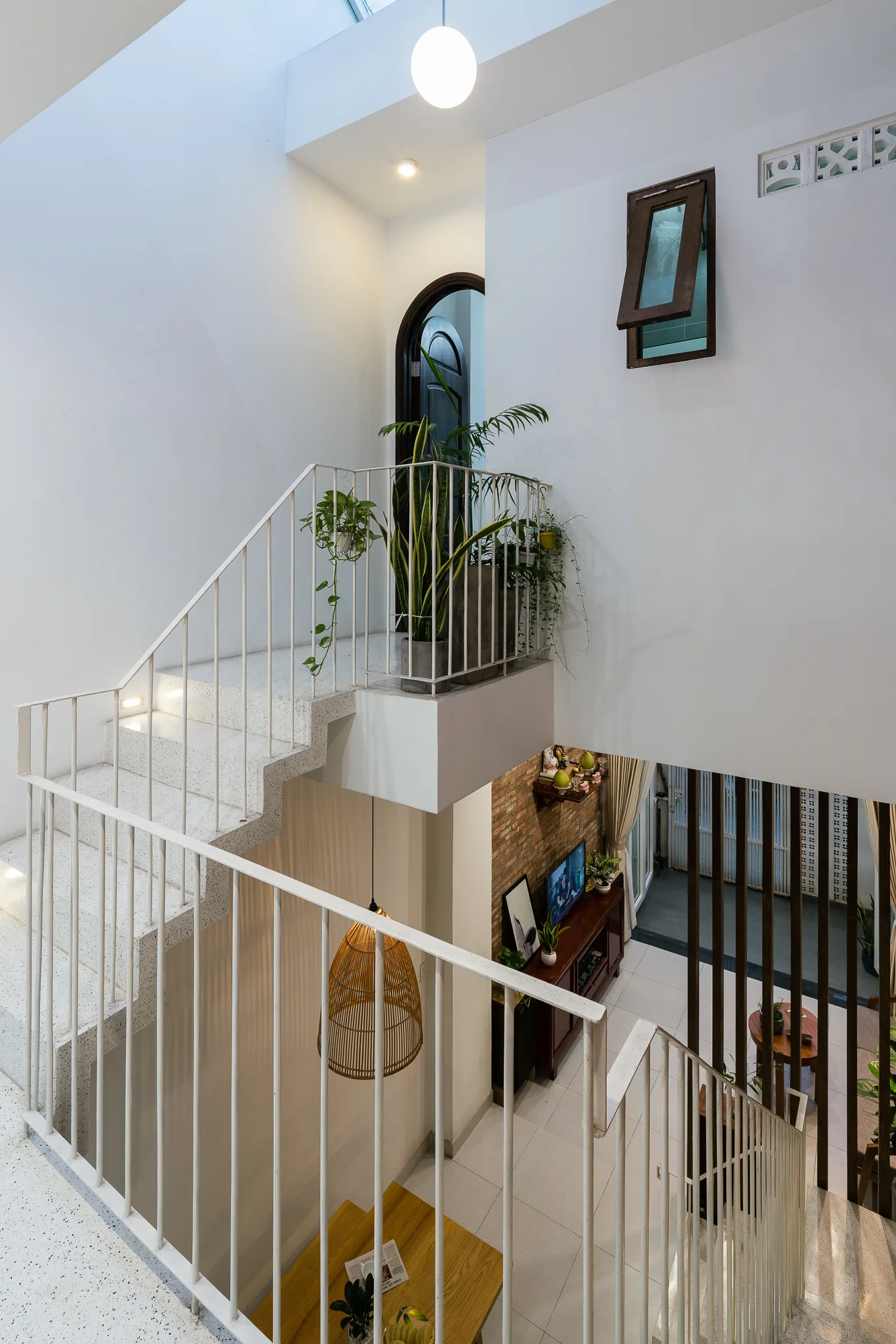 A multi-level home interior features a speckled white terrazzo staircase with a thin metal railing under a bright skylight.