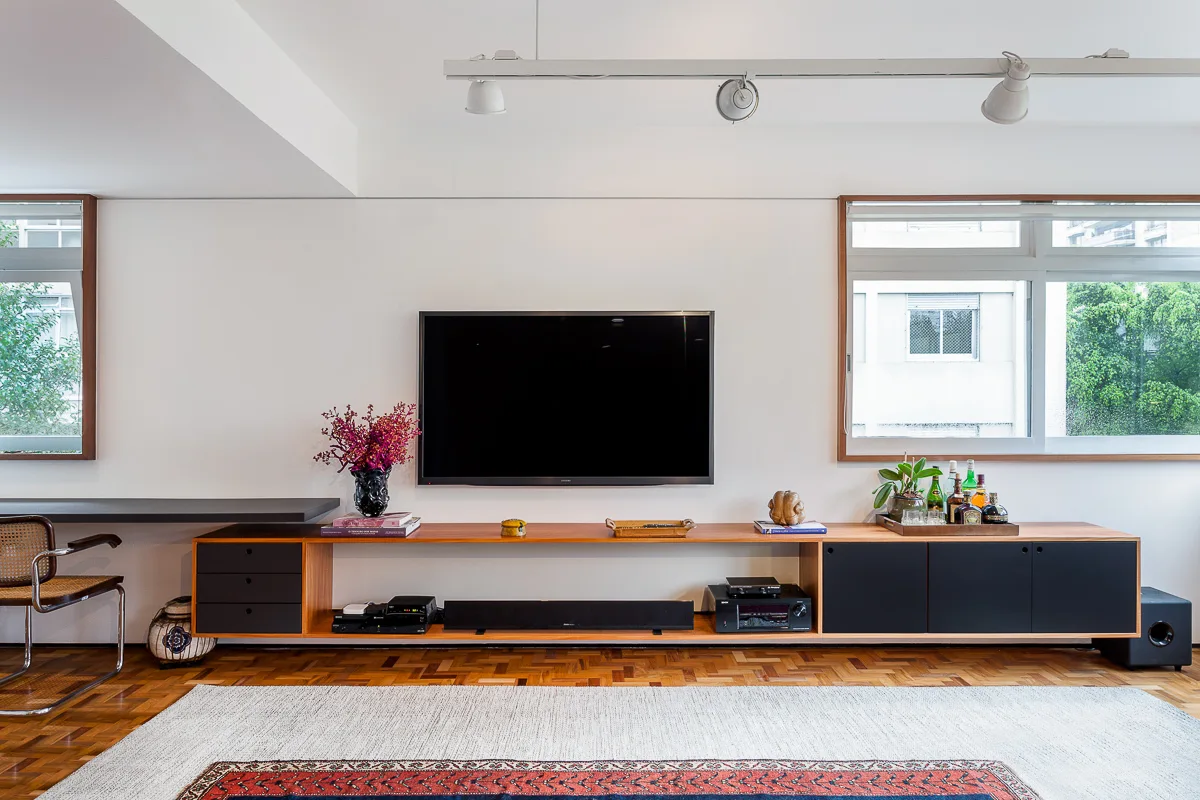 A modern living room features a long wall-mounted wooden media console beneath a TV, classic parquet wood flooring, and a large patterned area rug.