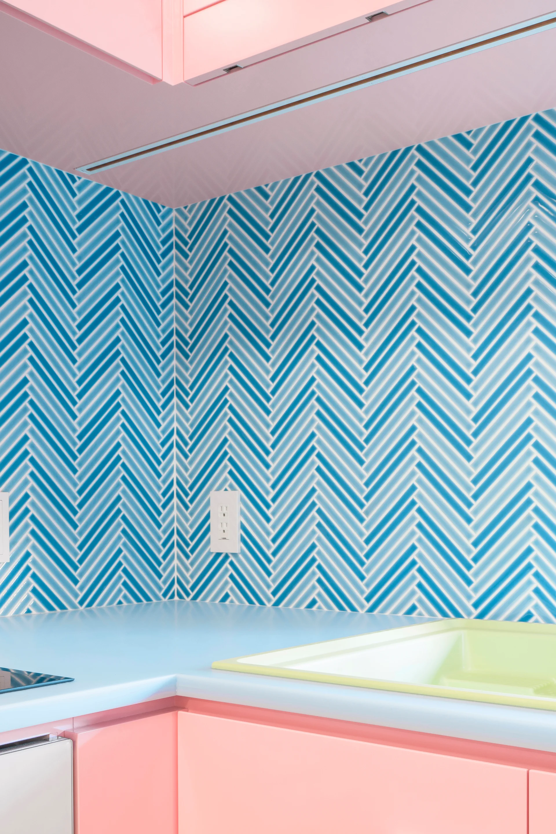A kitchen corner features pink cabinets, a light blue countertop with an integrated pale yellow sink, and a blue and white herringbone tile backsplash.