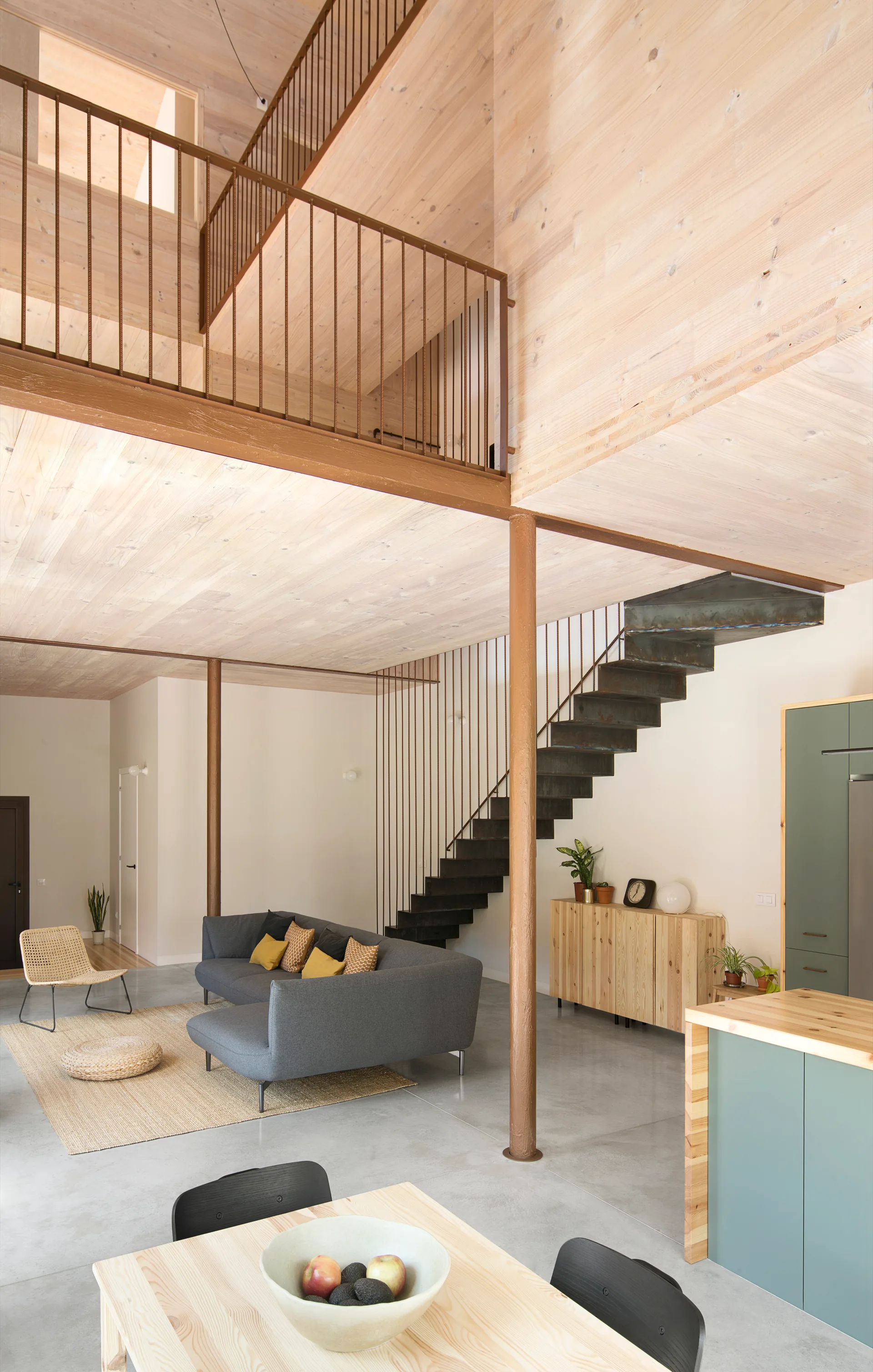 An open-plan living room features a grey sectional sofa, light wood-plank ceilings, and a black open-tread metal staircase leading to a mezzanine.
