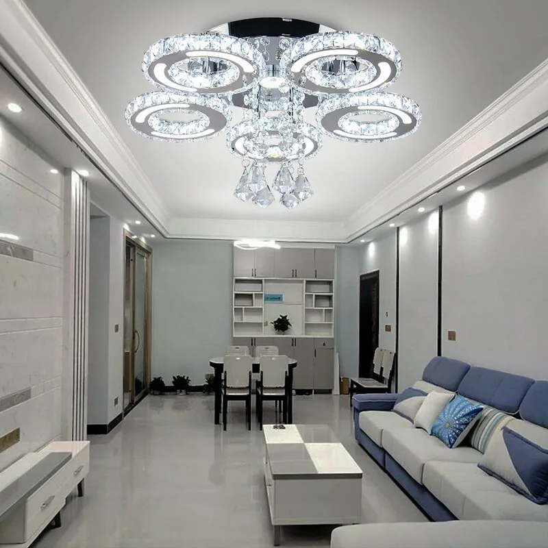 A modern living room features a blue and white sectional sofa, a glossy white tile floor, and a large decorative crystal ring chandelier.
