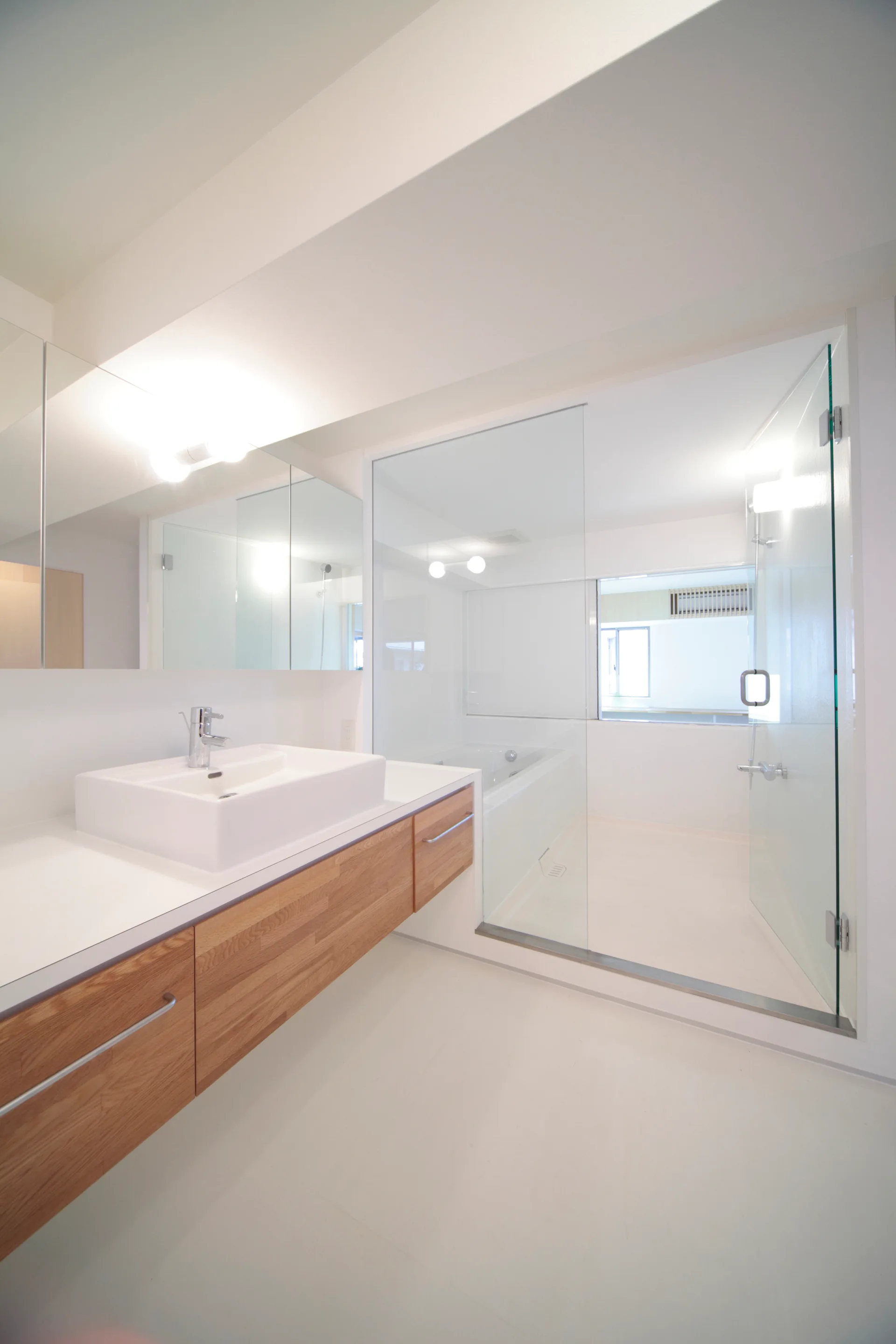 A modern bathroom features a floating wood-grain vanity with a white square sink, a large mirror, and a seamless glass shower enclosure.