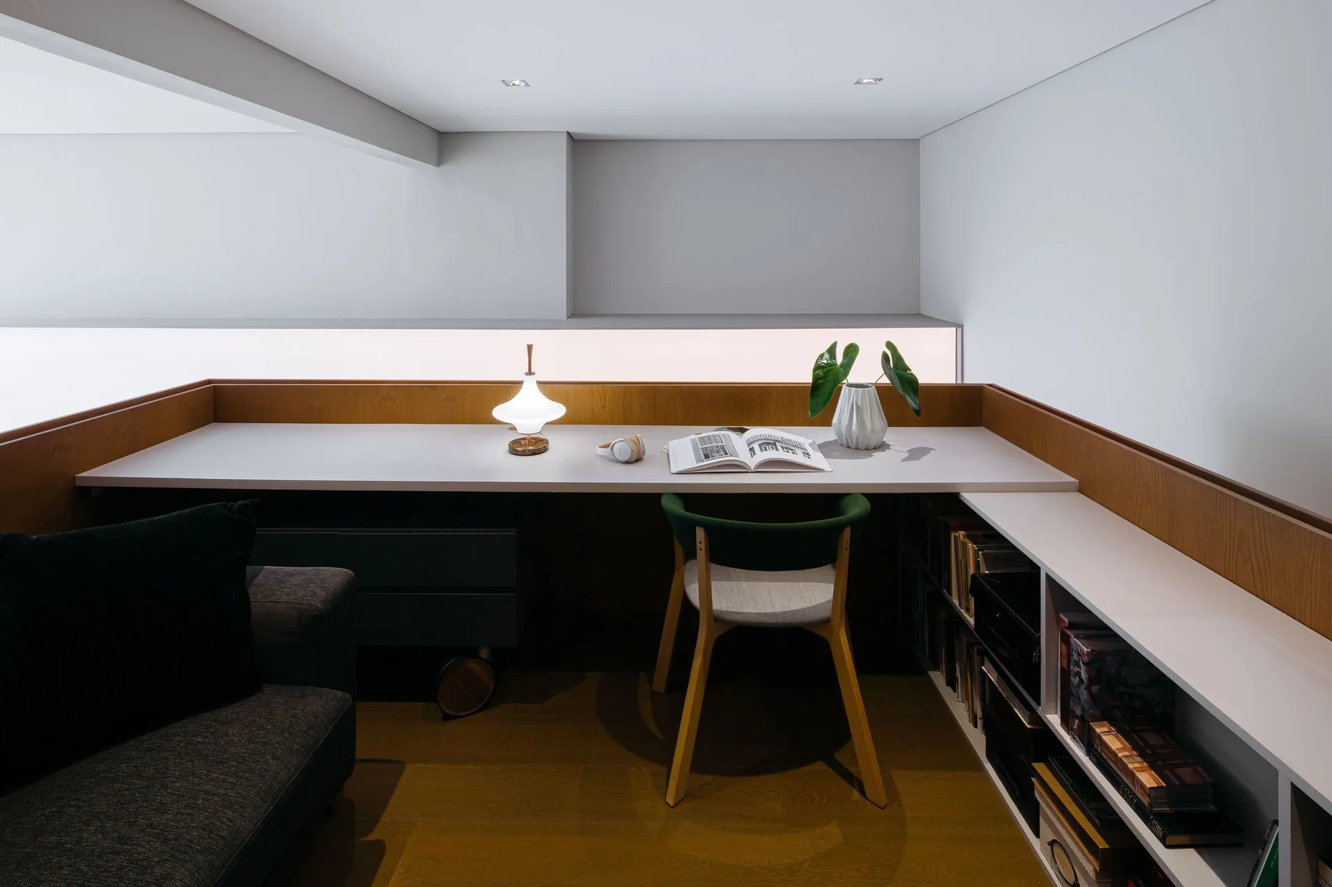 A modern home office corner featuring a long white built-in desk with wood trim, a green chair, and integrated low bookshelves.