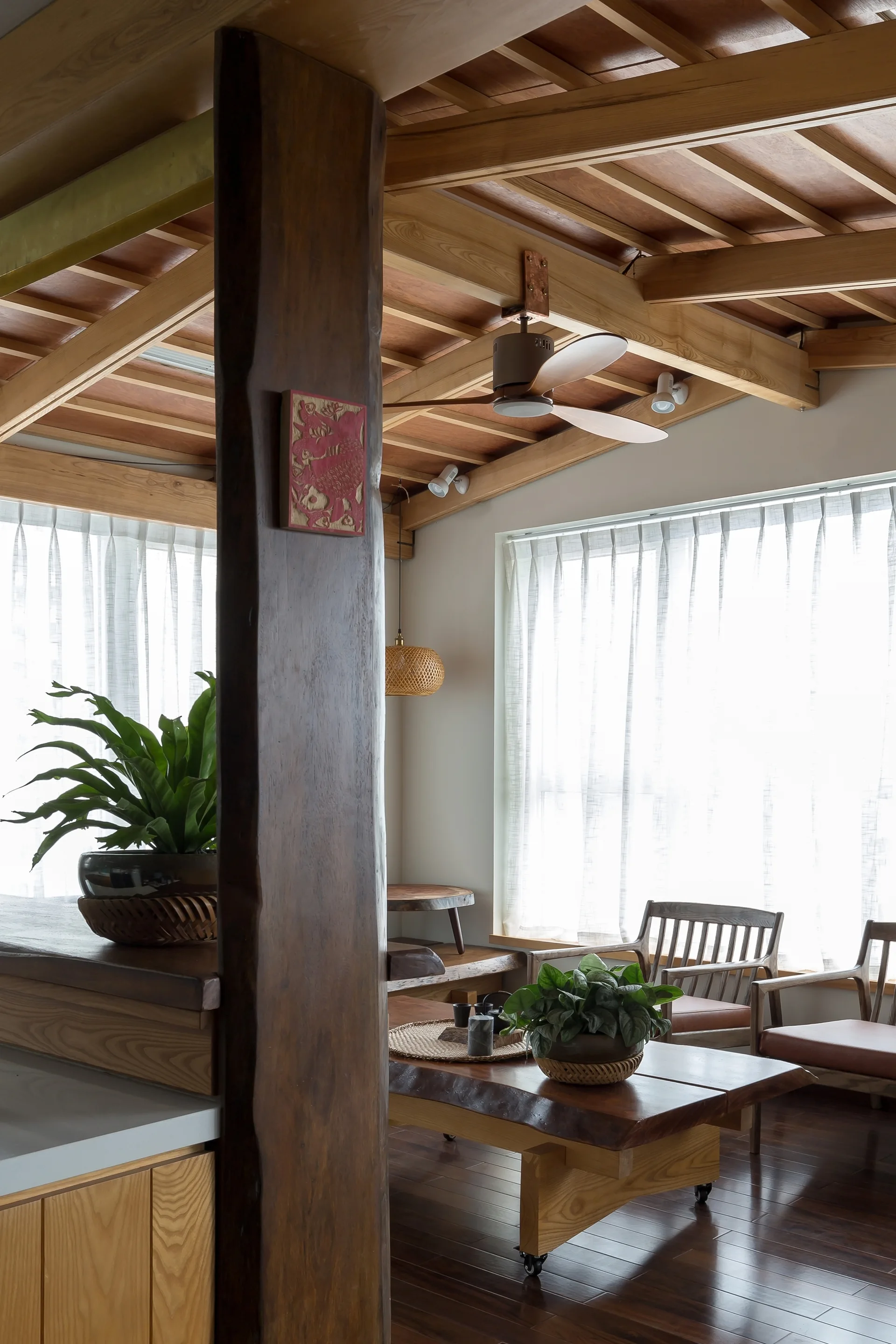 A Japandi living room featuring a timber support column, an exposed wood beamed ceiling, and a live-edge coffee table.