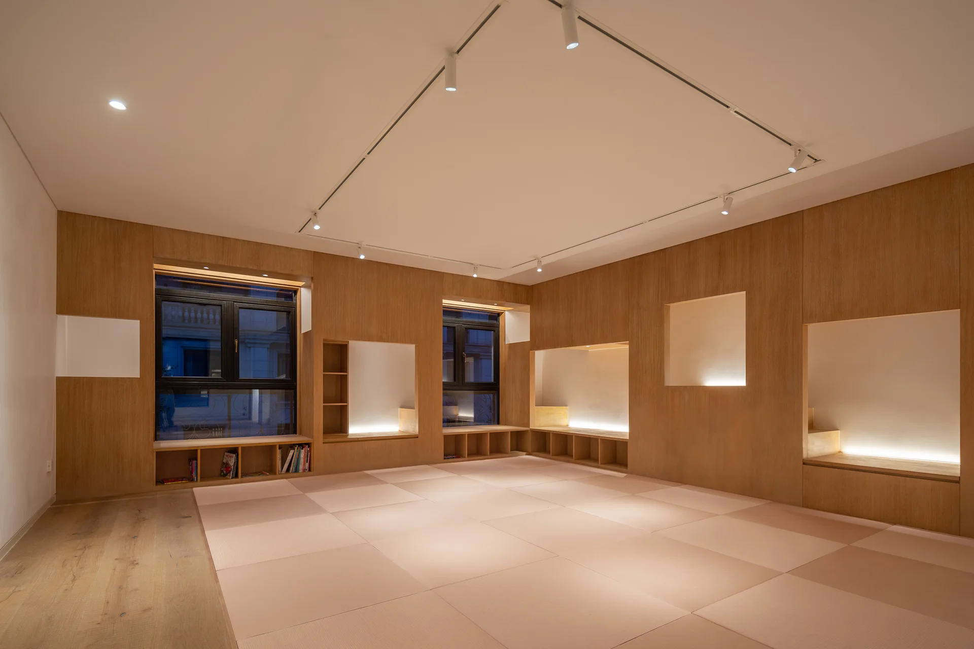 A minimalist room with light wood paneled walls, built-in recessed storage alcoves with soft lighting, and cream tatami mat flooring.