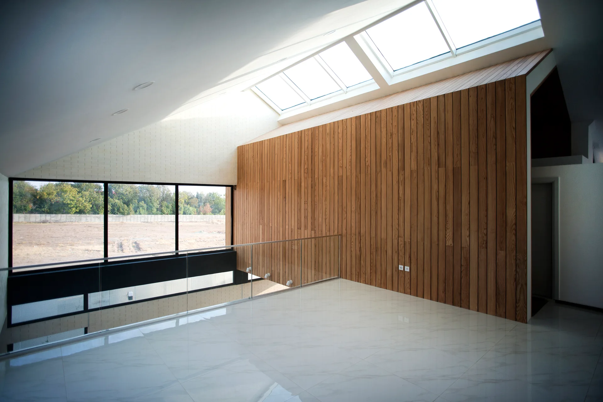 A minimalist home landing featuring a high slanted ceiling with integrated skylights, a vertical wood plank wall, and a polished tile floor.