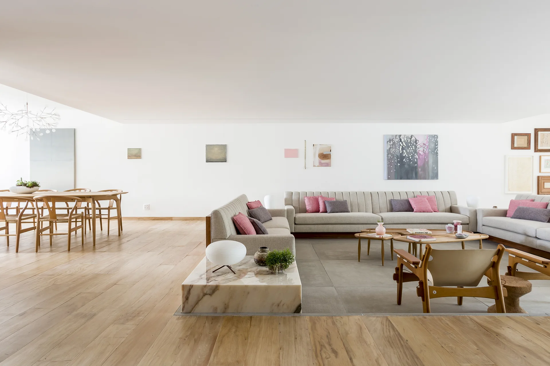 An open-concept living and dining area with a sunken lounge featuring grey sofas, light wood flooring, and a wooden dining table.