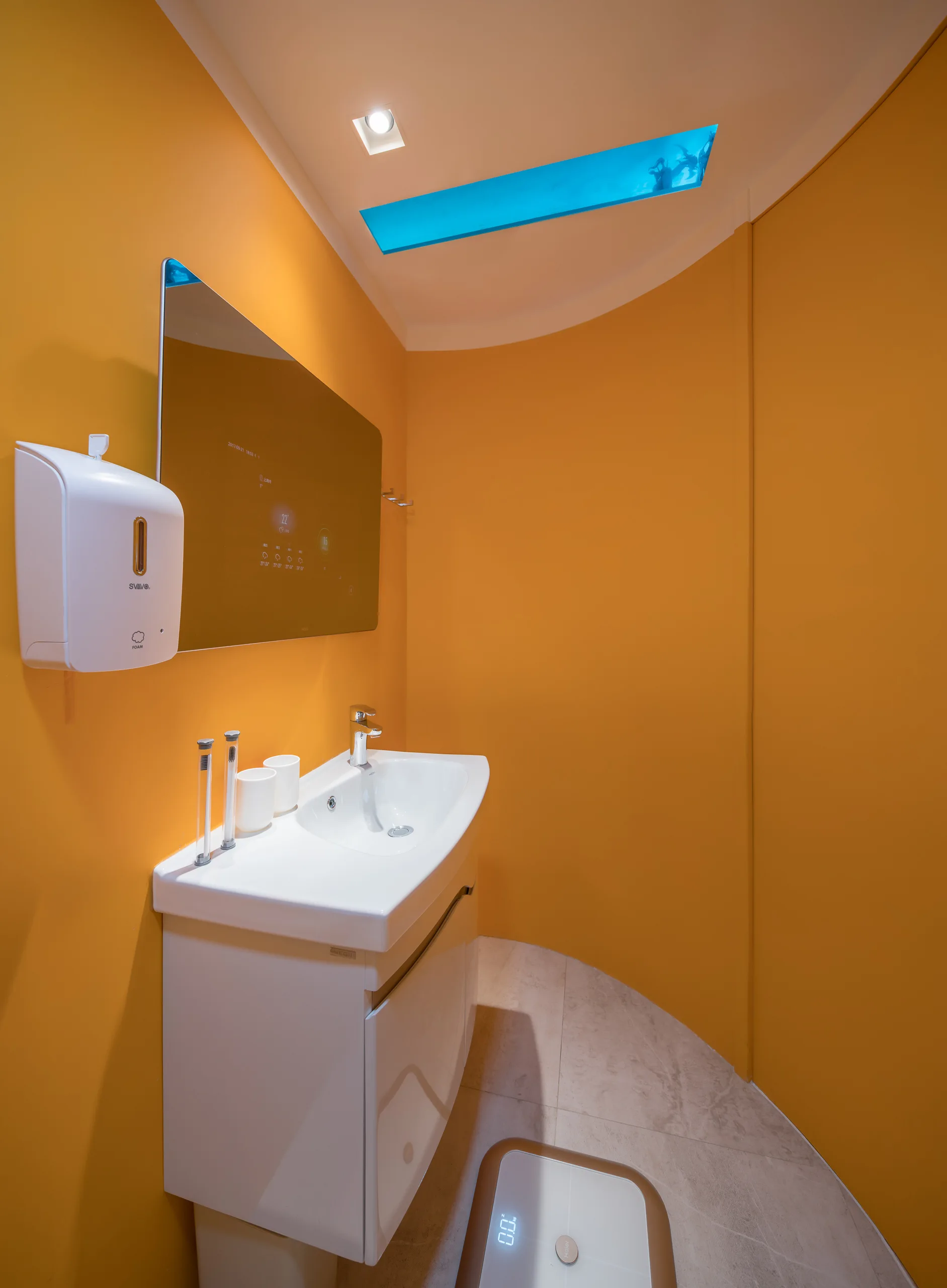A minimalist powder room features vibrant orange curved walls, a white ceramic sink vanity, a rectangular mirror, and a blue skylight panel.
