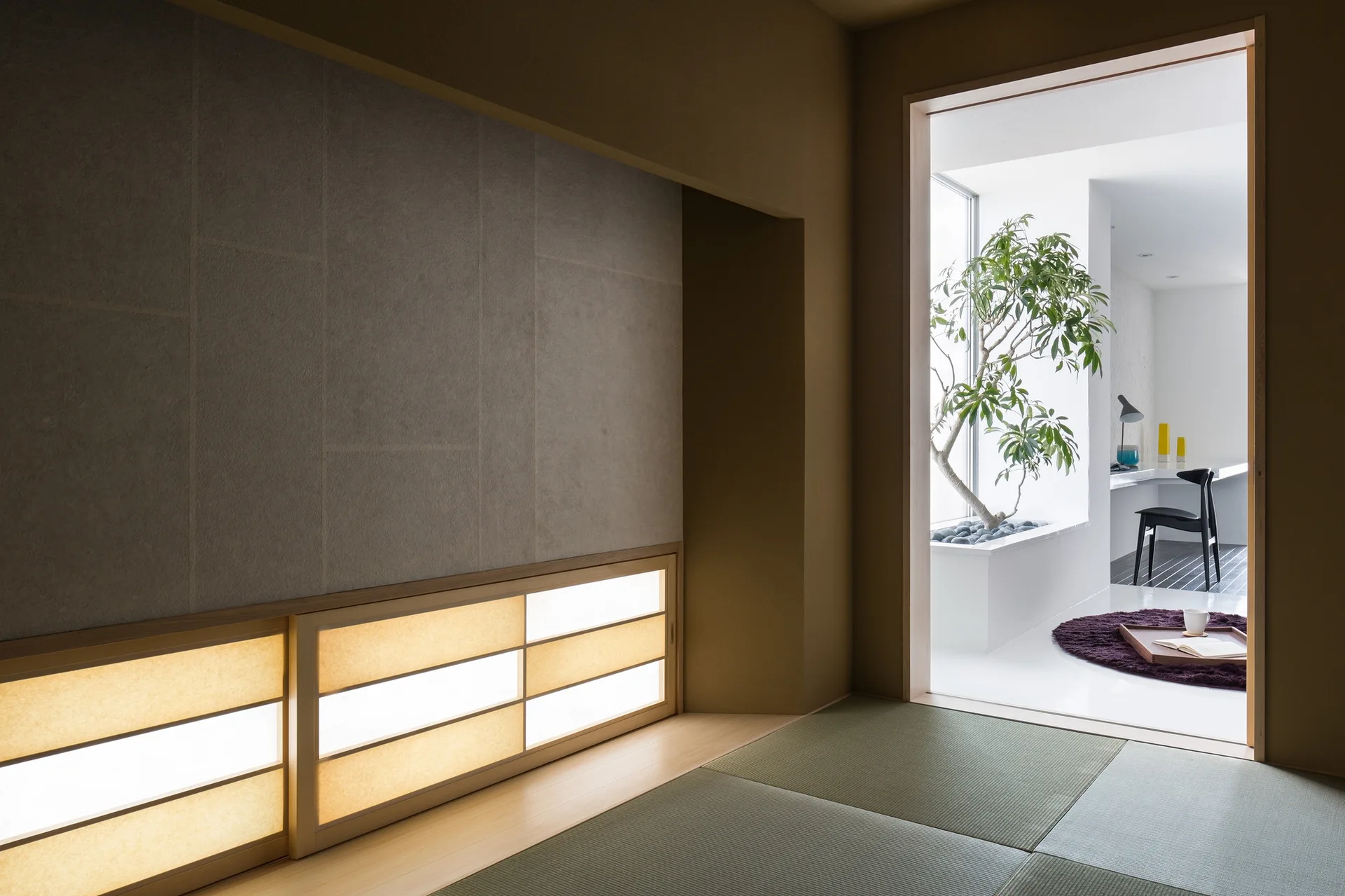 A traditional Japanese room with tatami mats and low illuminated shoji screens leads into a bright white minimalist workspace.