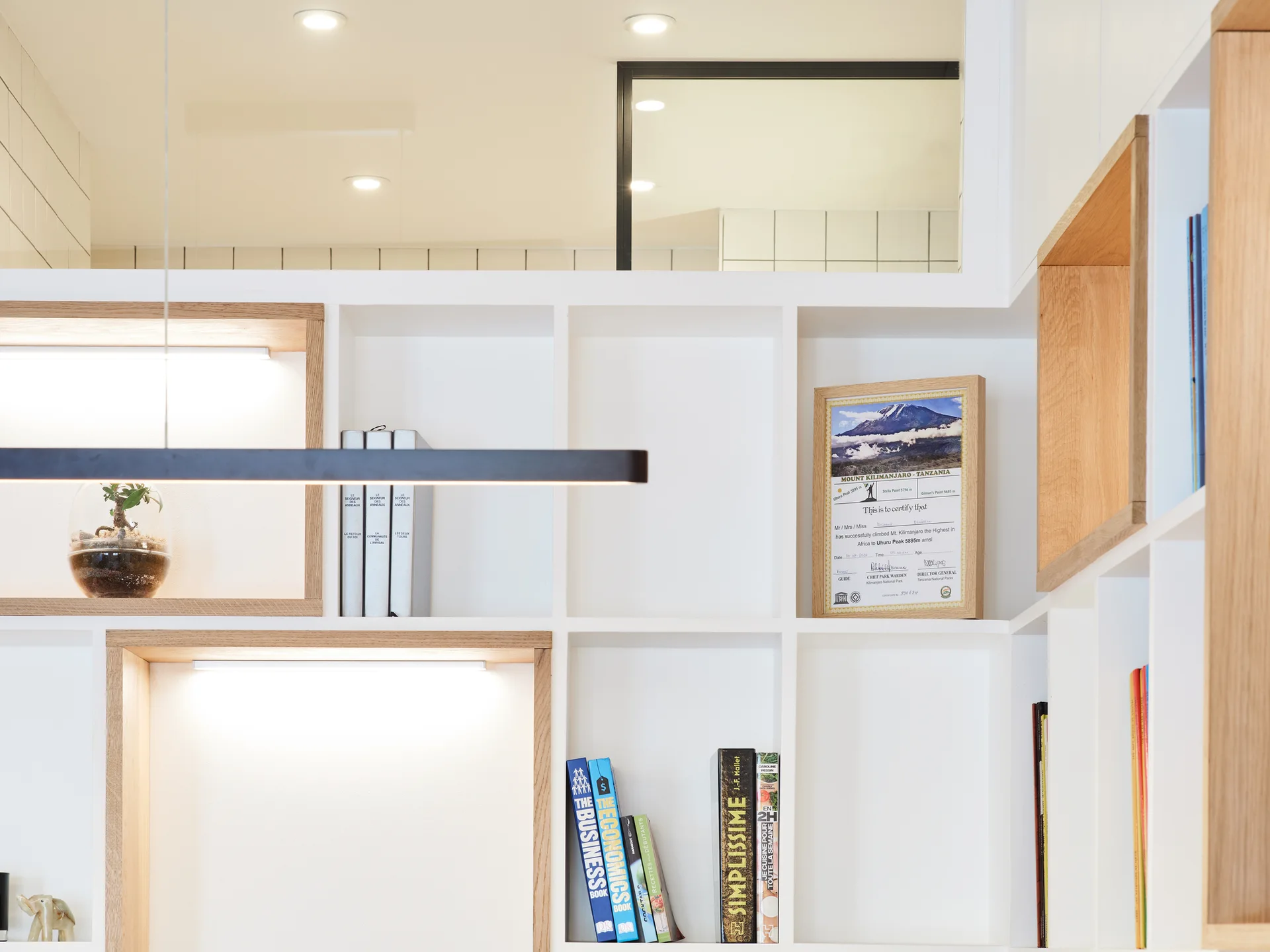 A white custom built-in shelving unit features selected oak-lined niches with integrated LED lighting, books, and framed art.