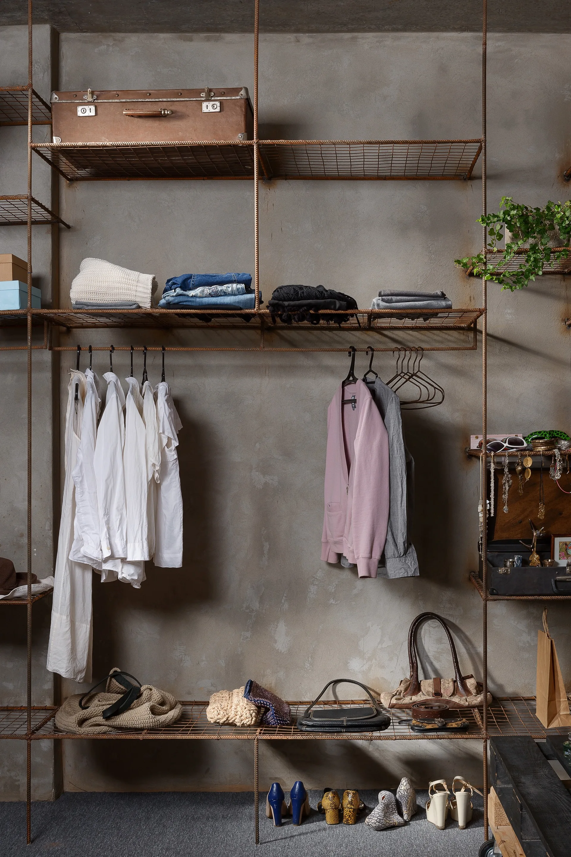 An industrial open closet organizer features rusted metal grid shelving and hanging rods mounted against an exposed grey concrete wall.