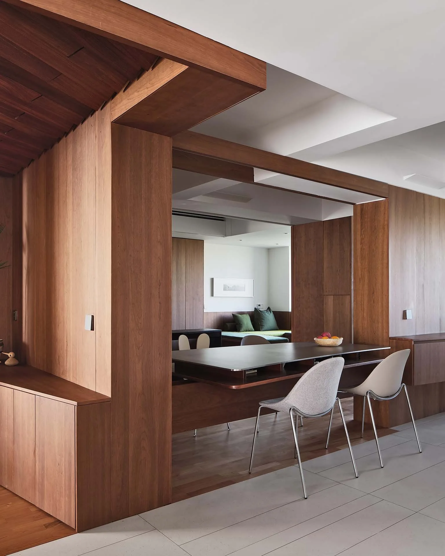 A contemporary dining room features warm wood-paneled walls, structural columns, and a dining table paired with minimalist modern chairs.