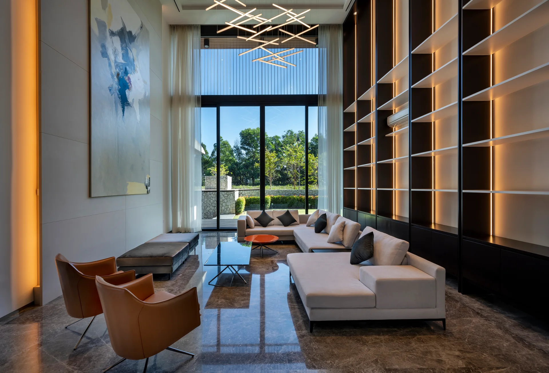 A double-height living room featuring a cream sectional sofa, tan leather armchairs, and a towering dark metal shelving unit with built-in LED lights.