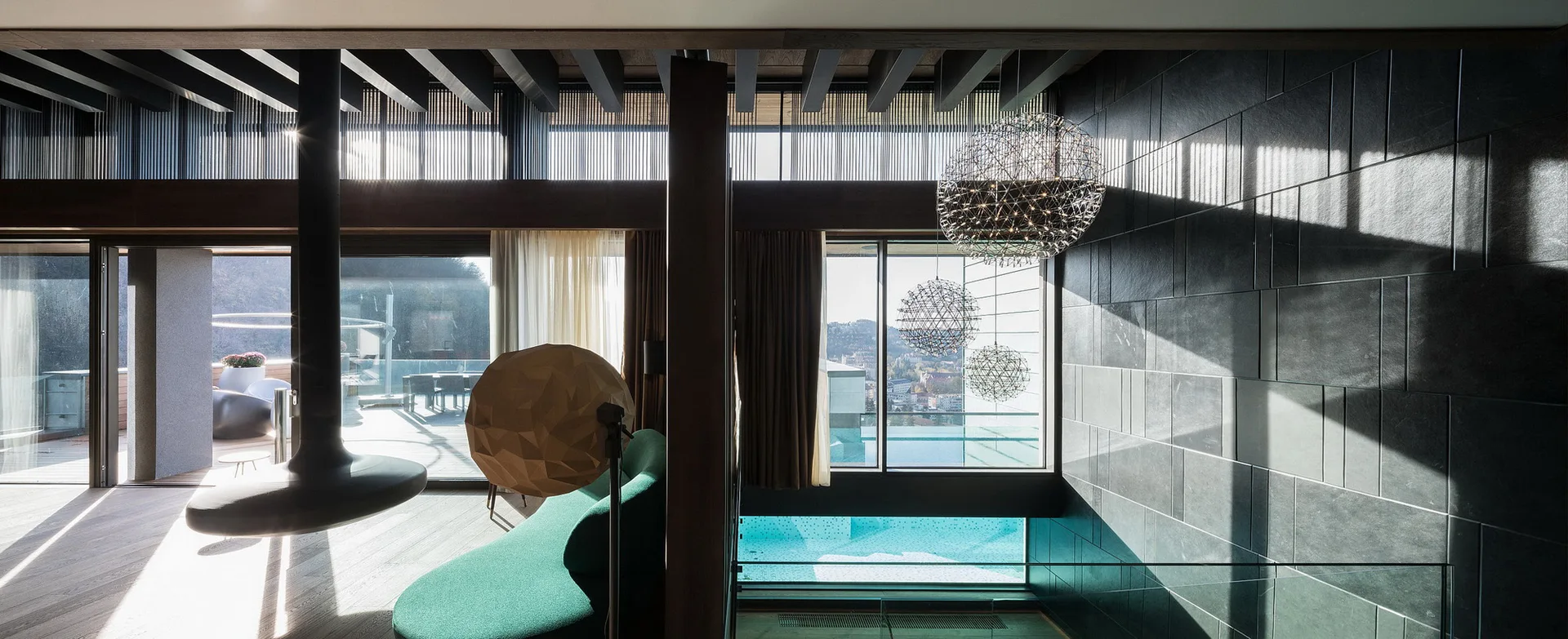 A contemporary living room features a curved green sofa, a black suspended fireplace, and a dark charcoal stone wall beside large windows.