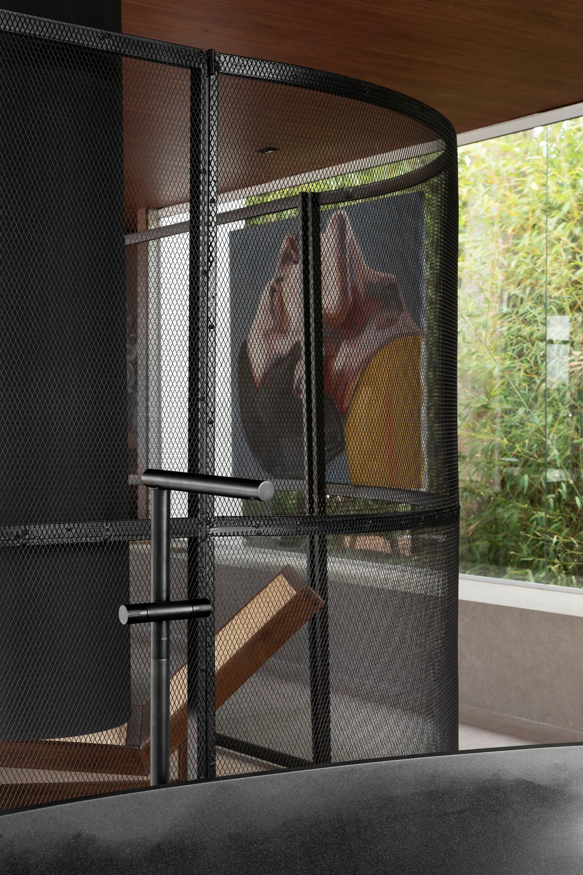 A modern matte black faucet stands in front of a curved black metal mesh screen inside a minimalist bathroom.