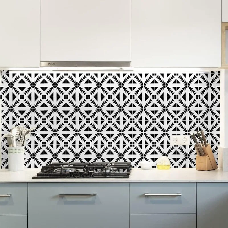 A modern kitchen counter with grey lower cabinets, a gas cooktop, and a high-contrast black and white geometric patterned tile backsplash.