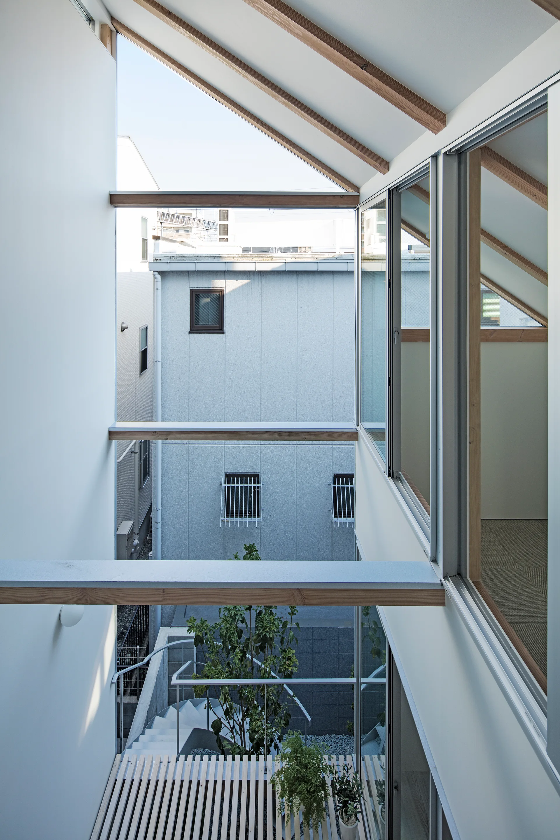 A modern interior light well features floor-to-ceiling windows, exposed wood ceiling beams, and a light wood slatted walkway overlooking a courtyard.