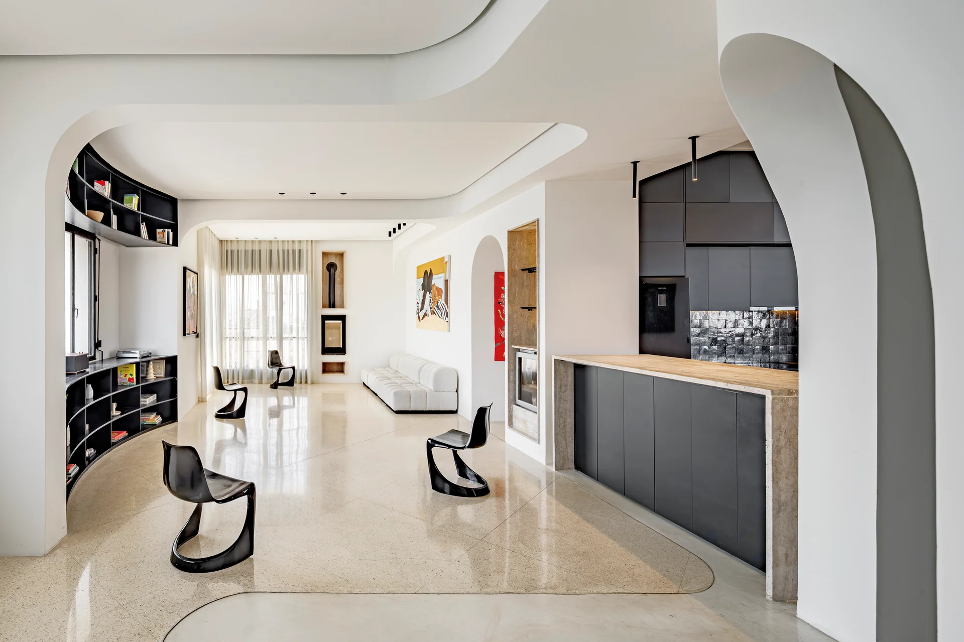 An open-concept living area features sweeping curved archways, black sculptural cantilevered chairs on polished stone floors, and a dark charcoal kitchen.