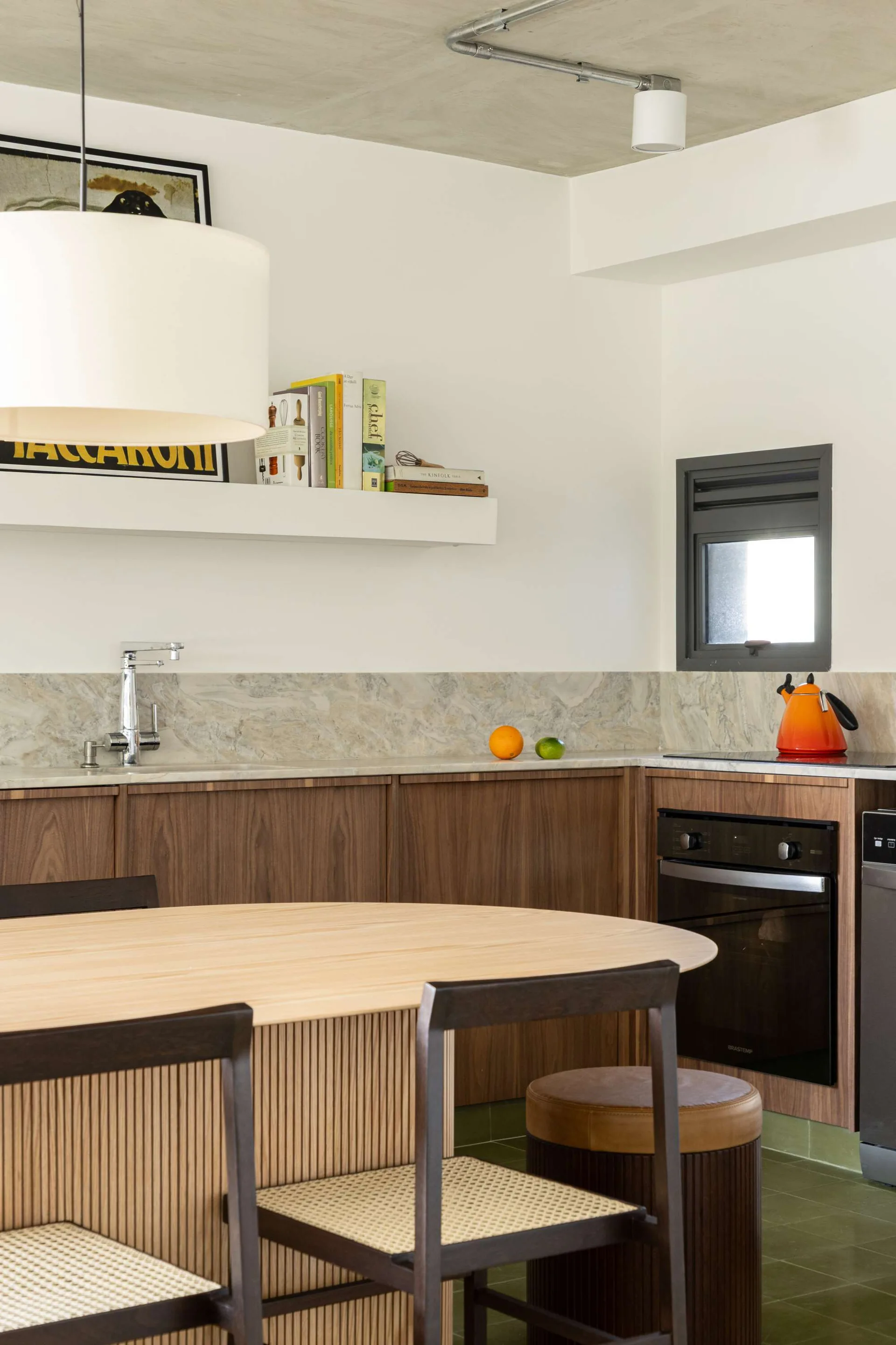 A modern kitchen features wood-toned base cabinets with a stone backsplash, a light wood oval dining table with cane chairs, and a white floating shelf.