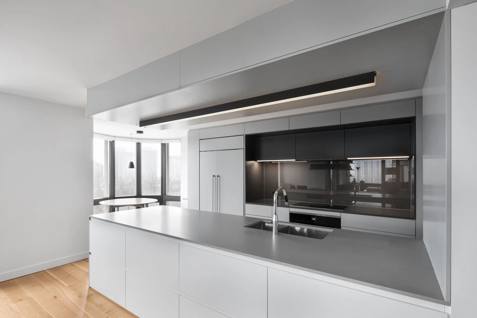 A minimalist kitchen featuring flat-panel grey cabinetry, a large matching island with a double sink, and a black linear pendant light.